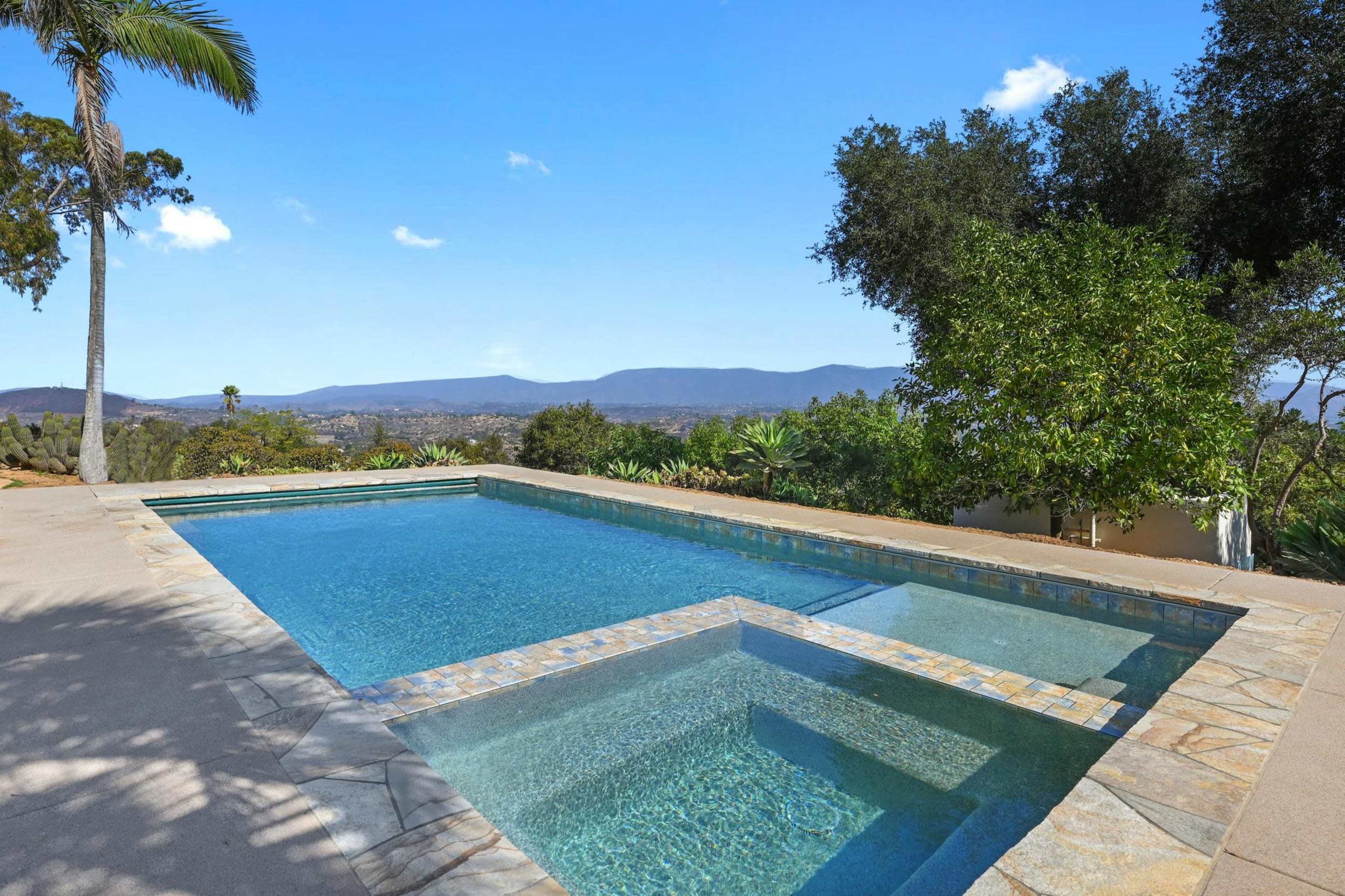 A rectangular swimming pool surrounded by a concrete deck and overlooking a mountainous landscape.