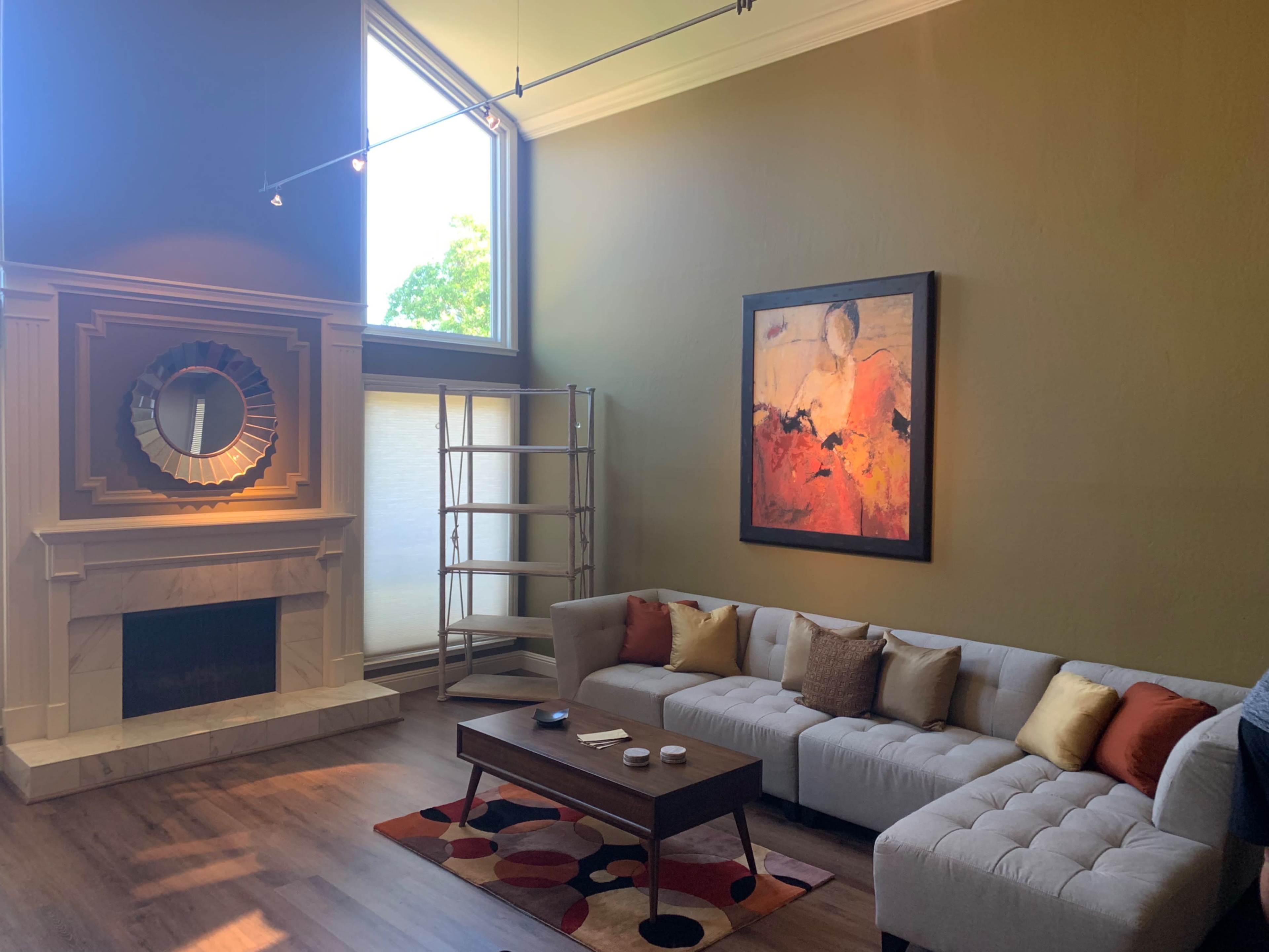 A modern living room featuring a light-colored sectional sofa, a wooden coffee table, a large abstract painting, and a fireplace.