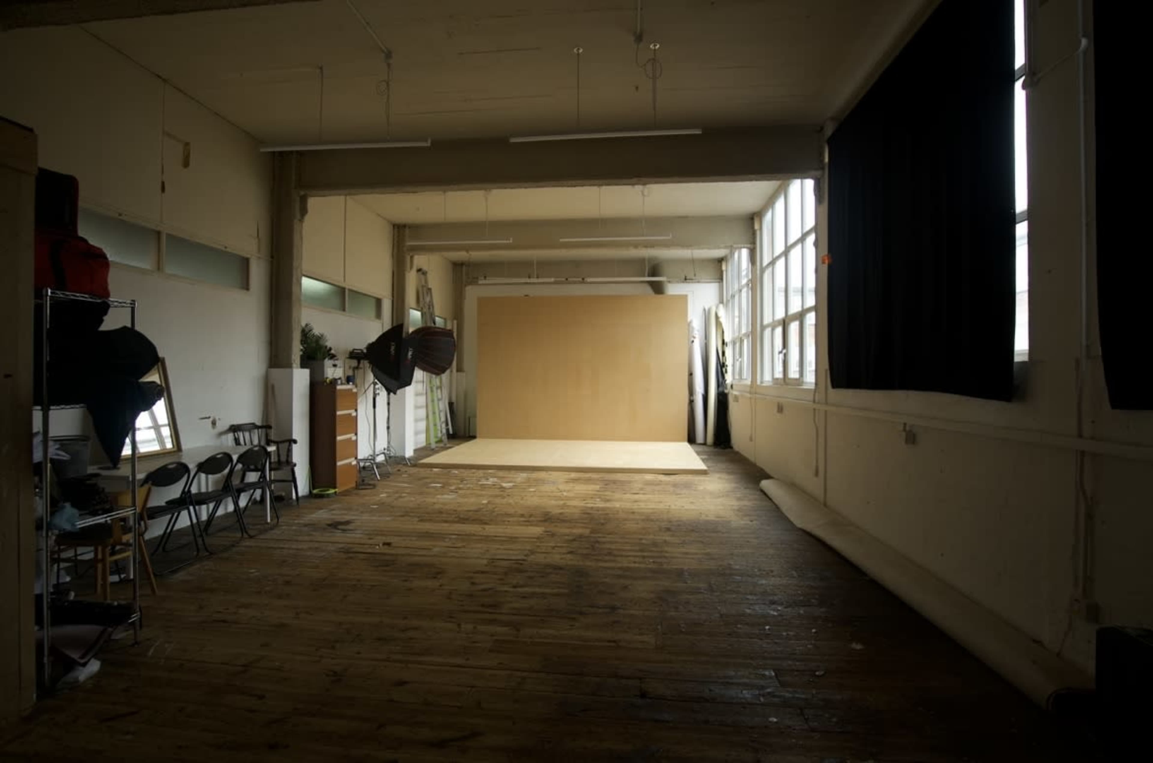A spacious interior with wooden floors, large windows, and a blank backdrop set against a wall, ideal for photography or art projects.