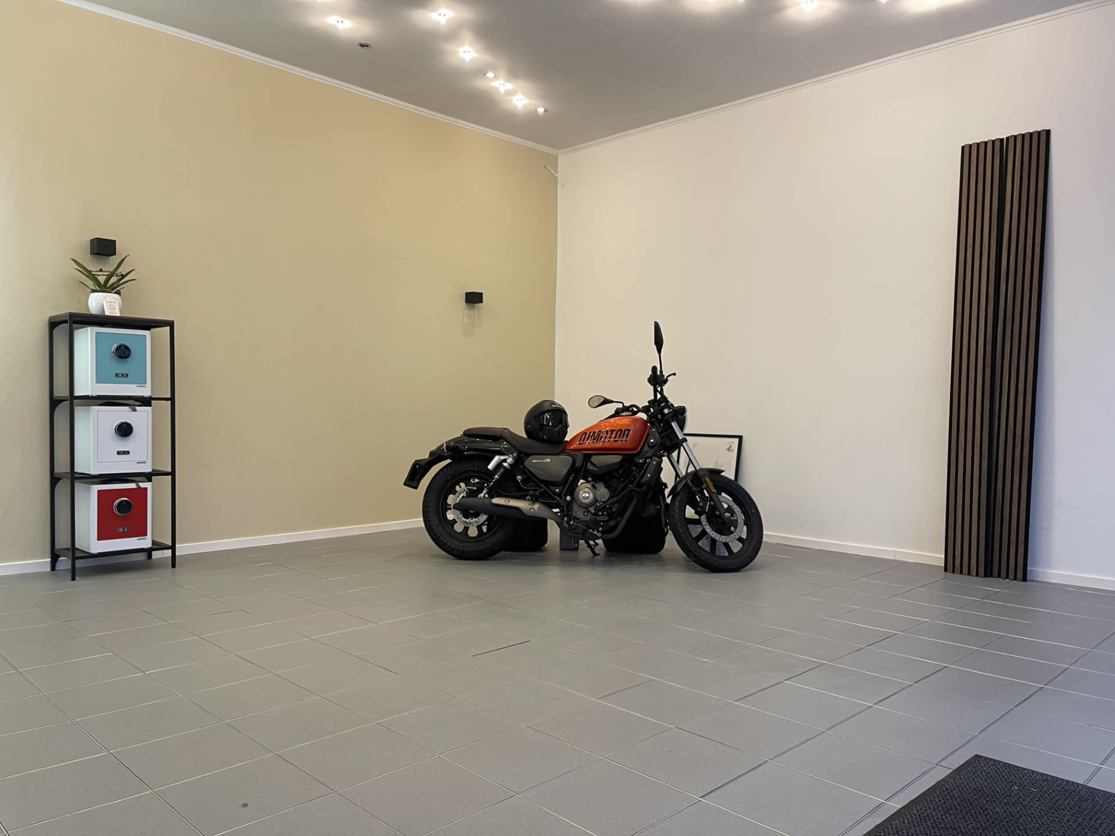 A motorcycle is parked in a spacious, minimalistic room with a few decorative items and a small shelf.