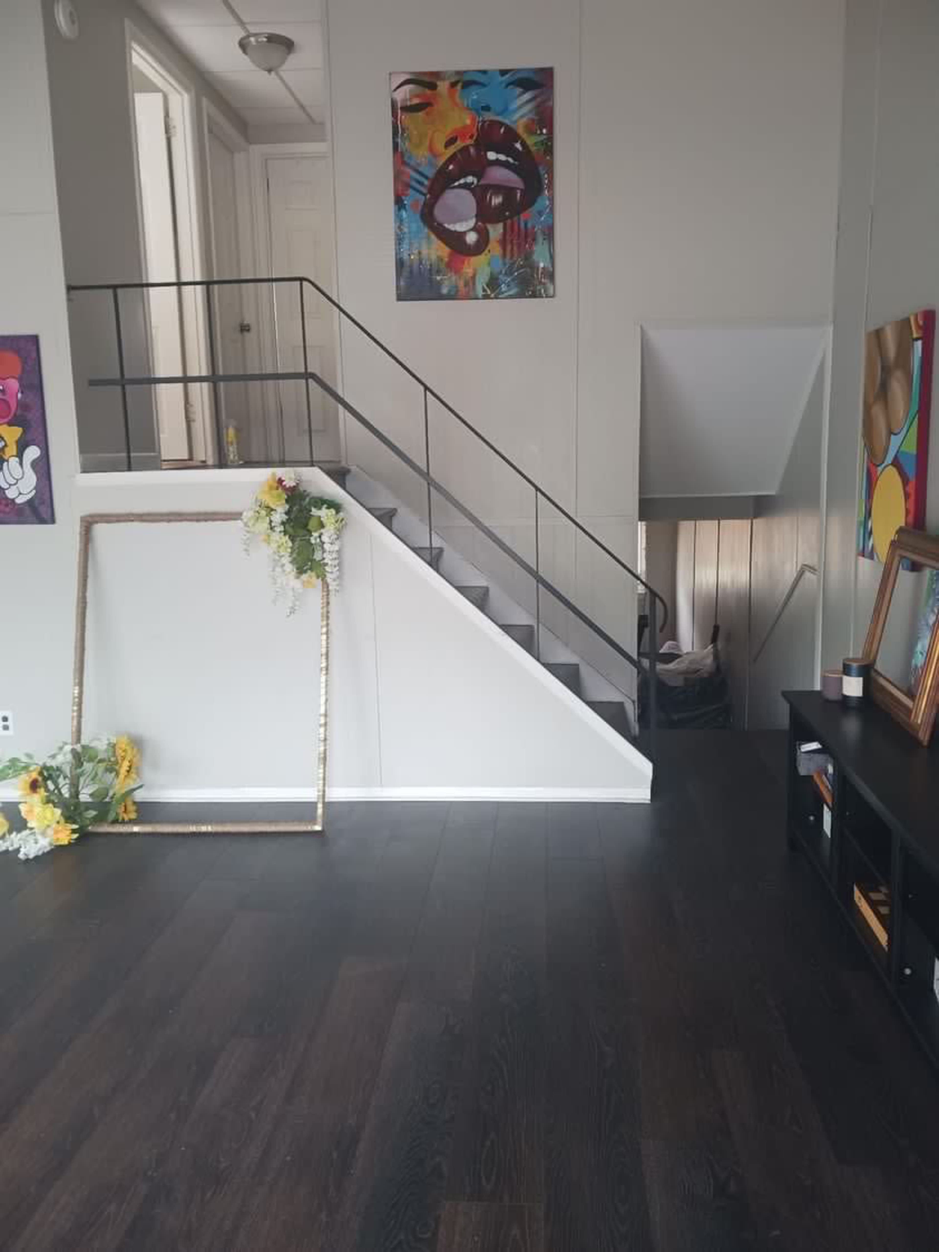 A modern interior with a staircase leading to an upper level, adorned with colorful wall art and a decorative empty frame on the floor.