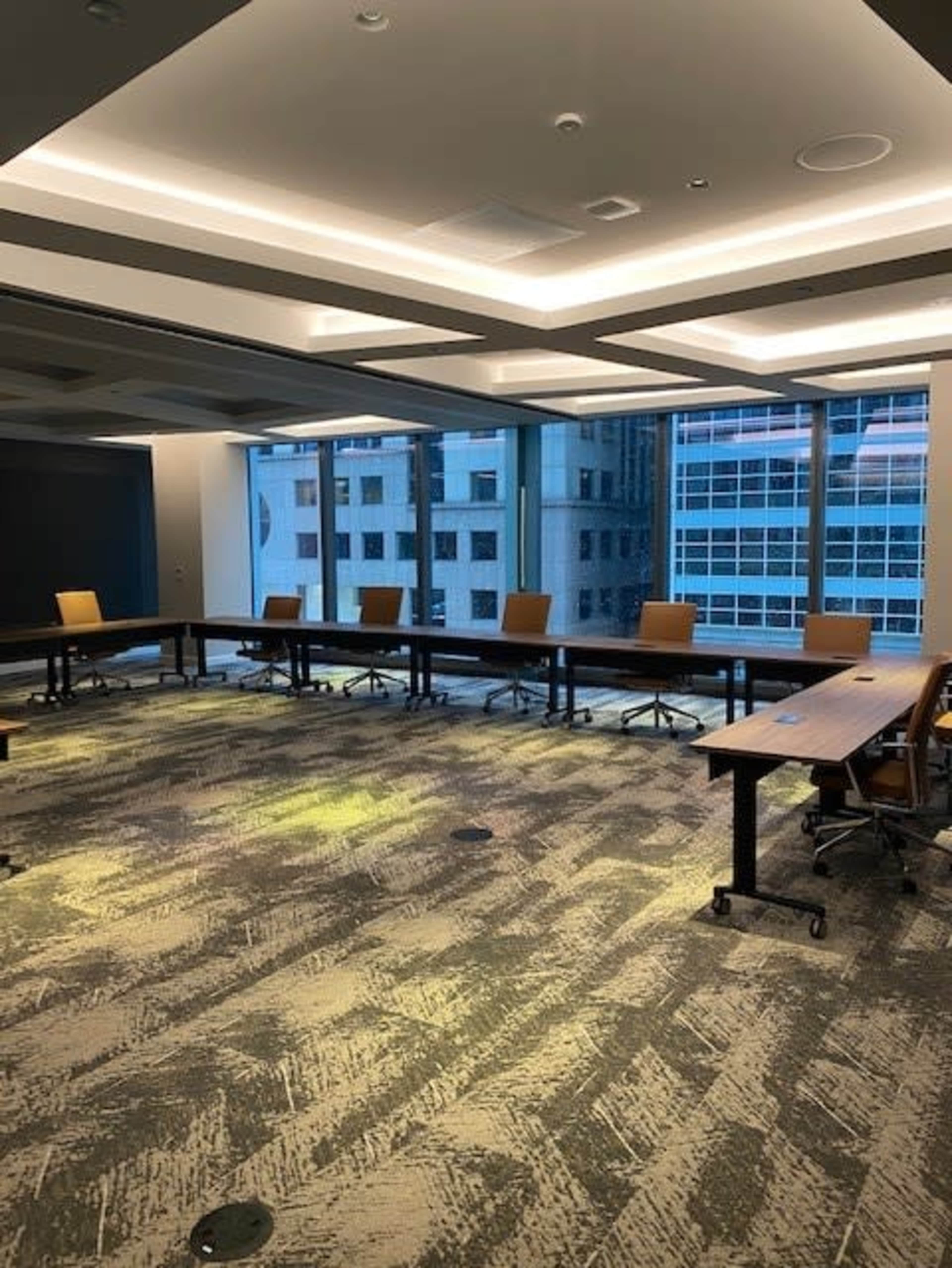 A conference room with a circular table setup, featuring several brown chairs and large windows displaying a view of neighboring buildings.