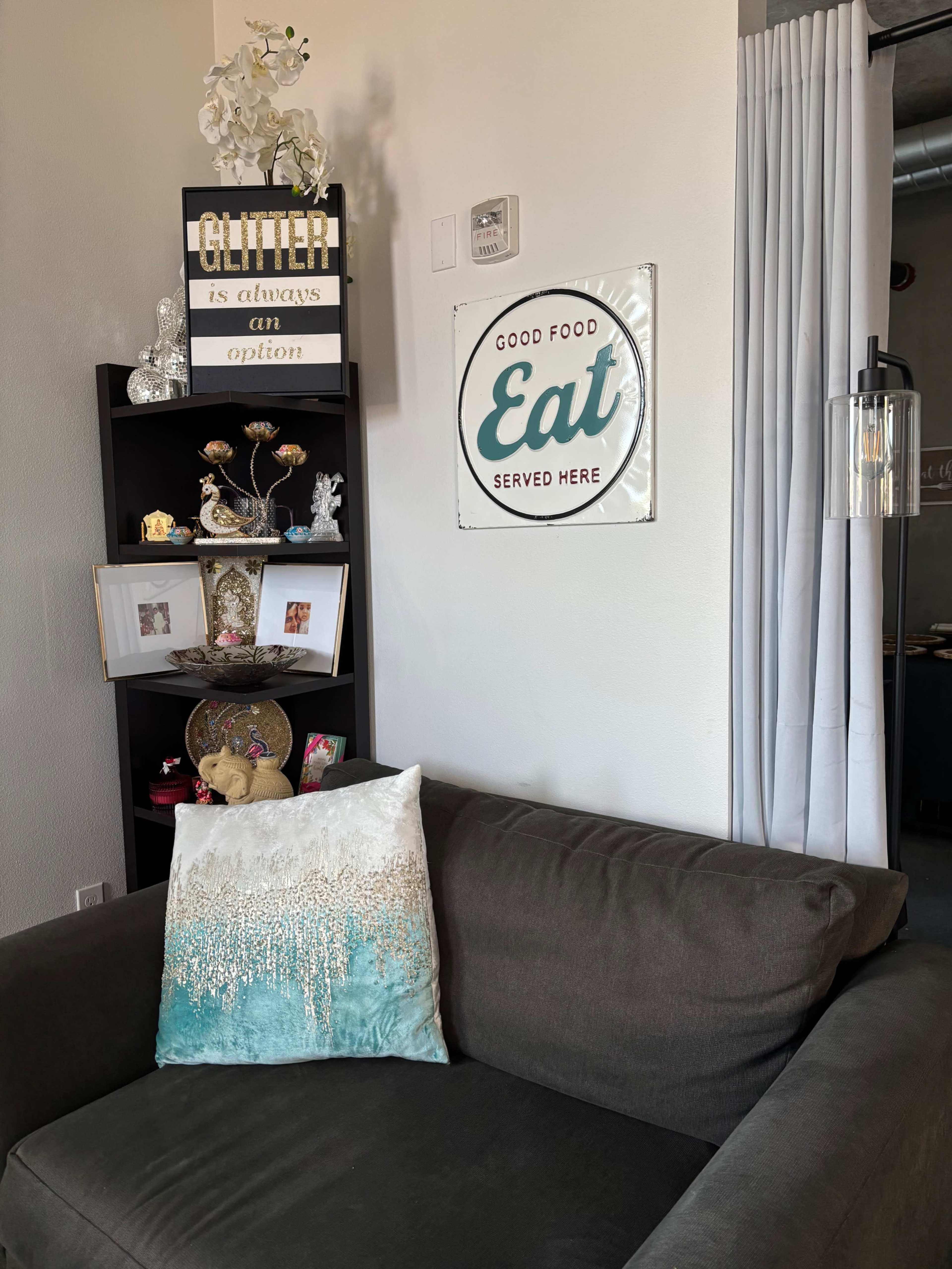 A gray couch sits next to a black shelf displaying decorative items and a sign that reads "GOOD FOOD Eat SERVED HERE."