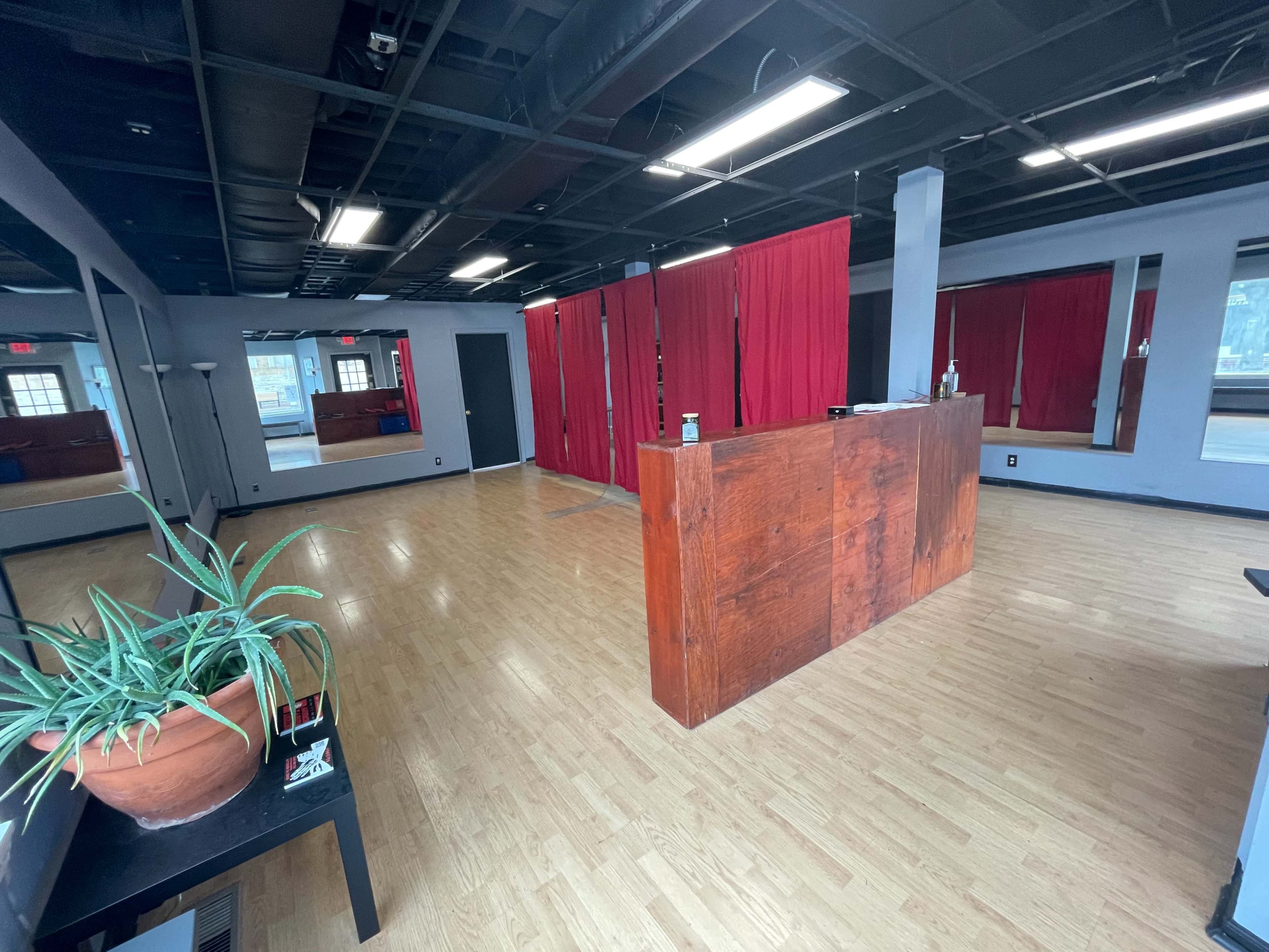 An empty studio space with wooden flooring, a reception area made of wood, and red curtains separating different sections.