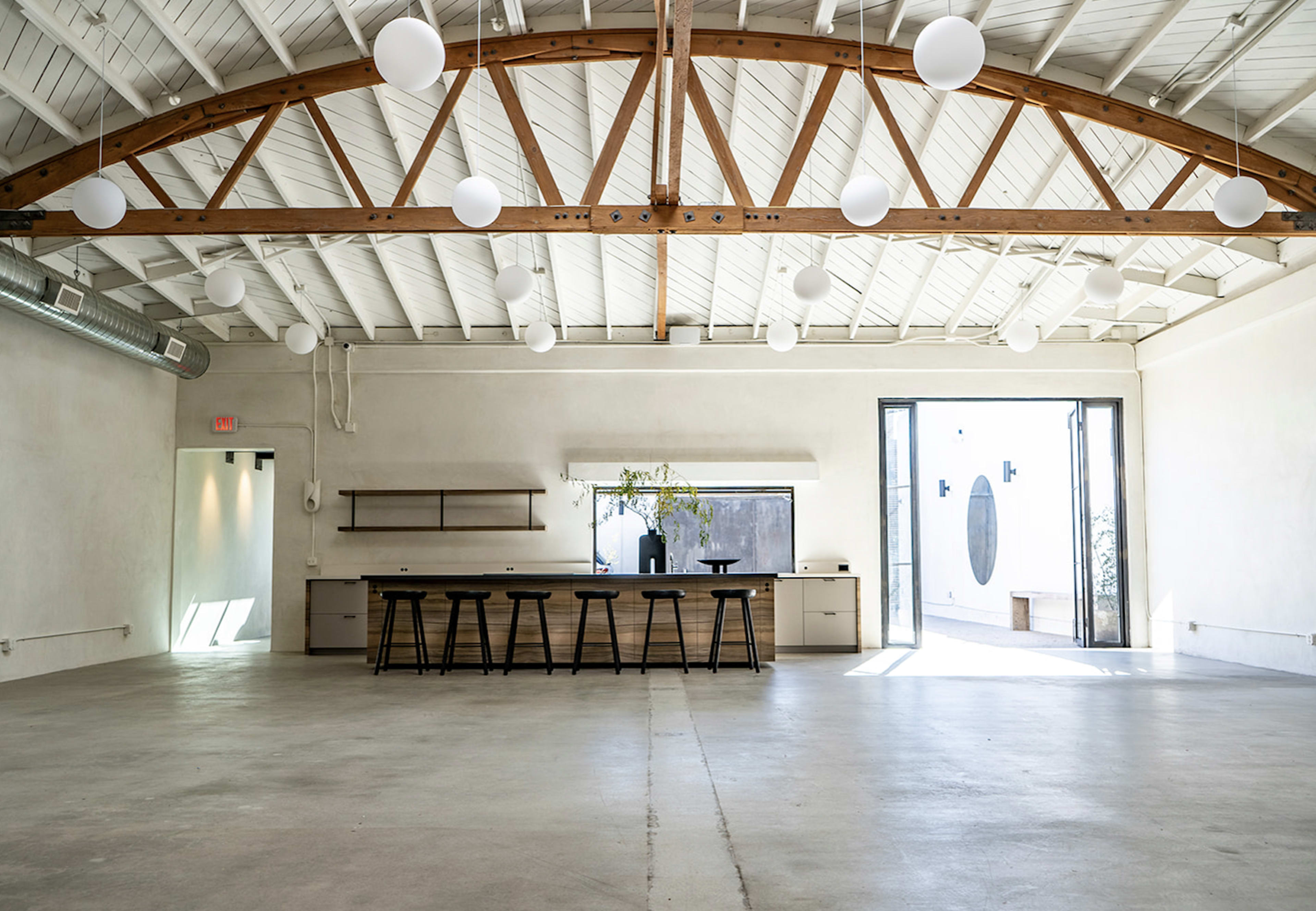 A spacious, minimalist interior with concrete flooring, a wooden beam ceiling, and a long counter with stools.