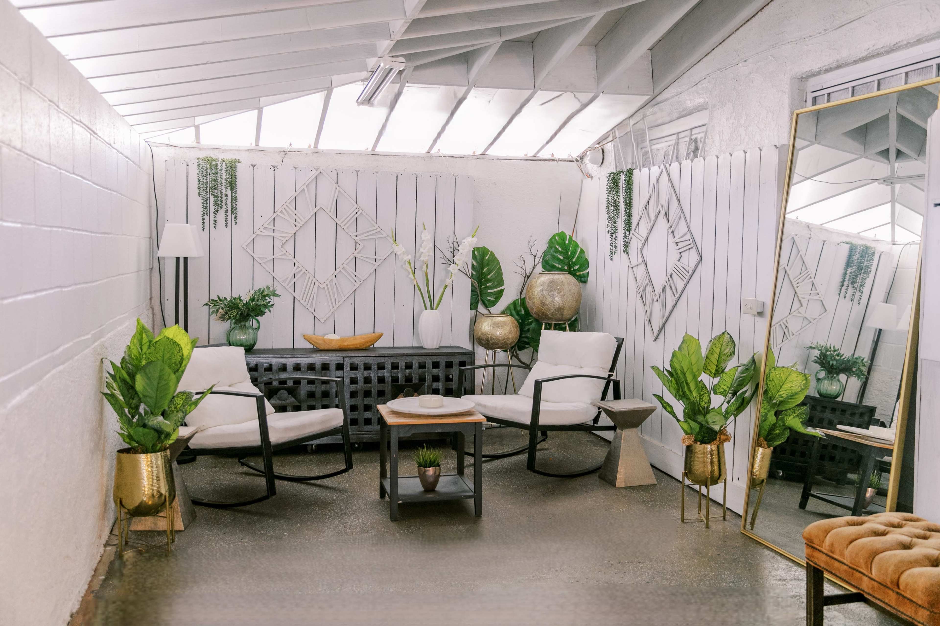 A minimalist indoor seating area with two chairs, a coffee table, decorative plants, and mirrors against a white-paneled wall.