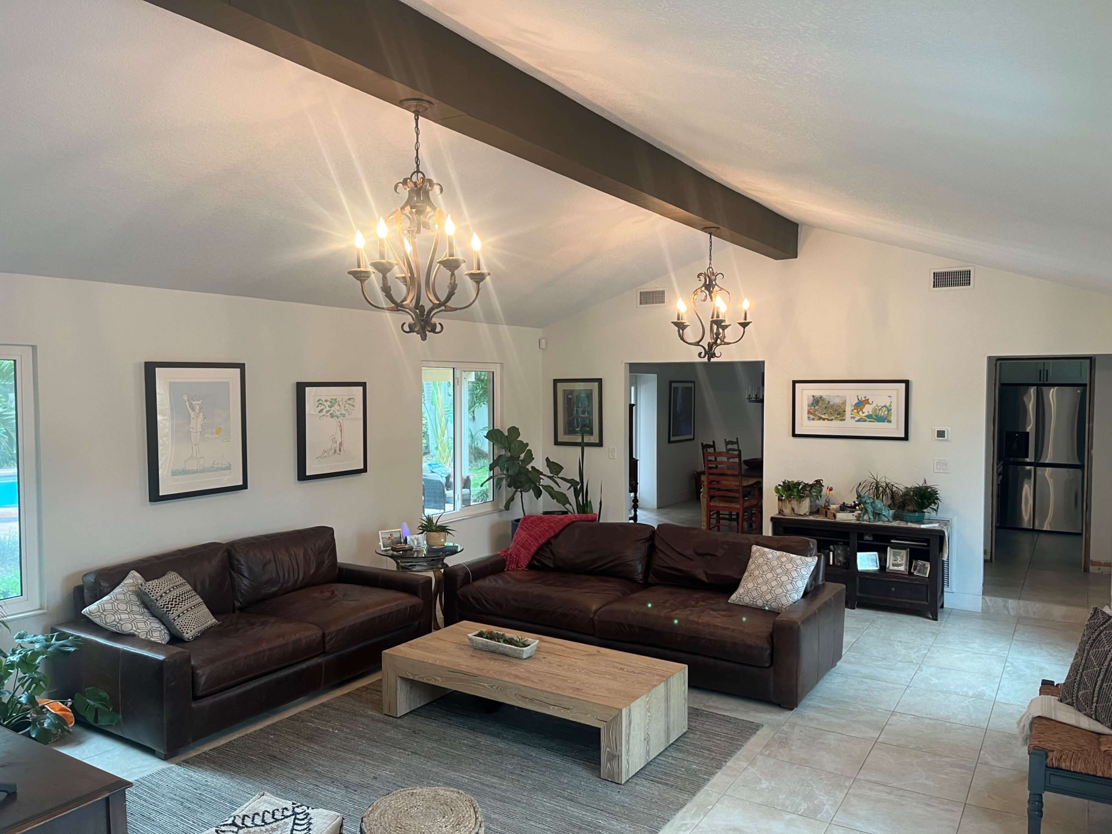 The cozy living room features two brown leather sofas, a wooden coffee table, and large windows that overlook a pool area.