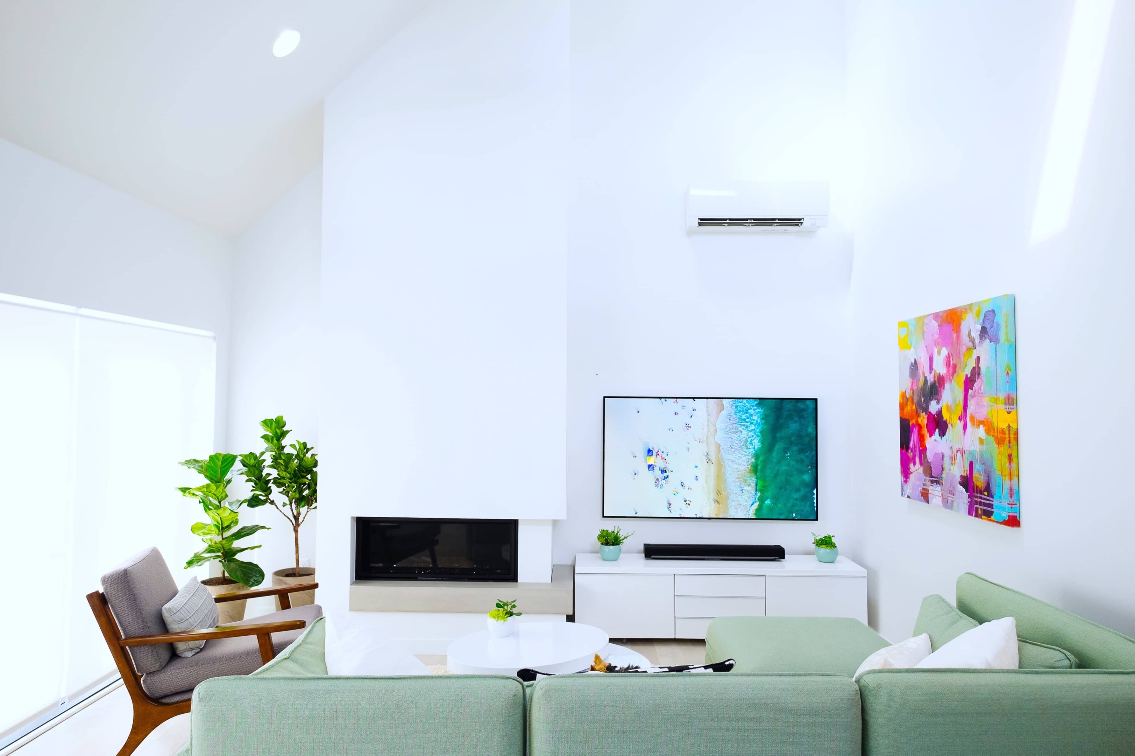 The room features a modern living space with a large TV mounted on the wall, a white sectional sofa, a coffee table, and a potted plant.