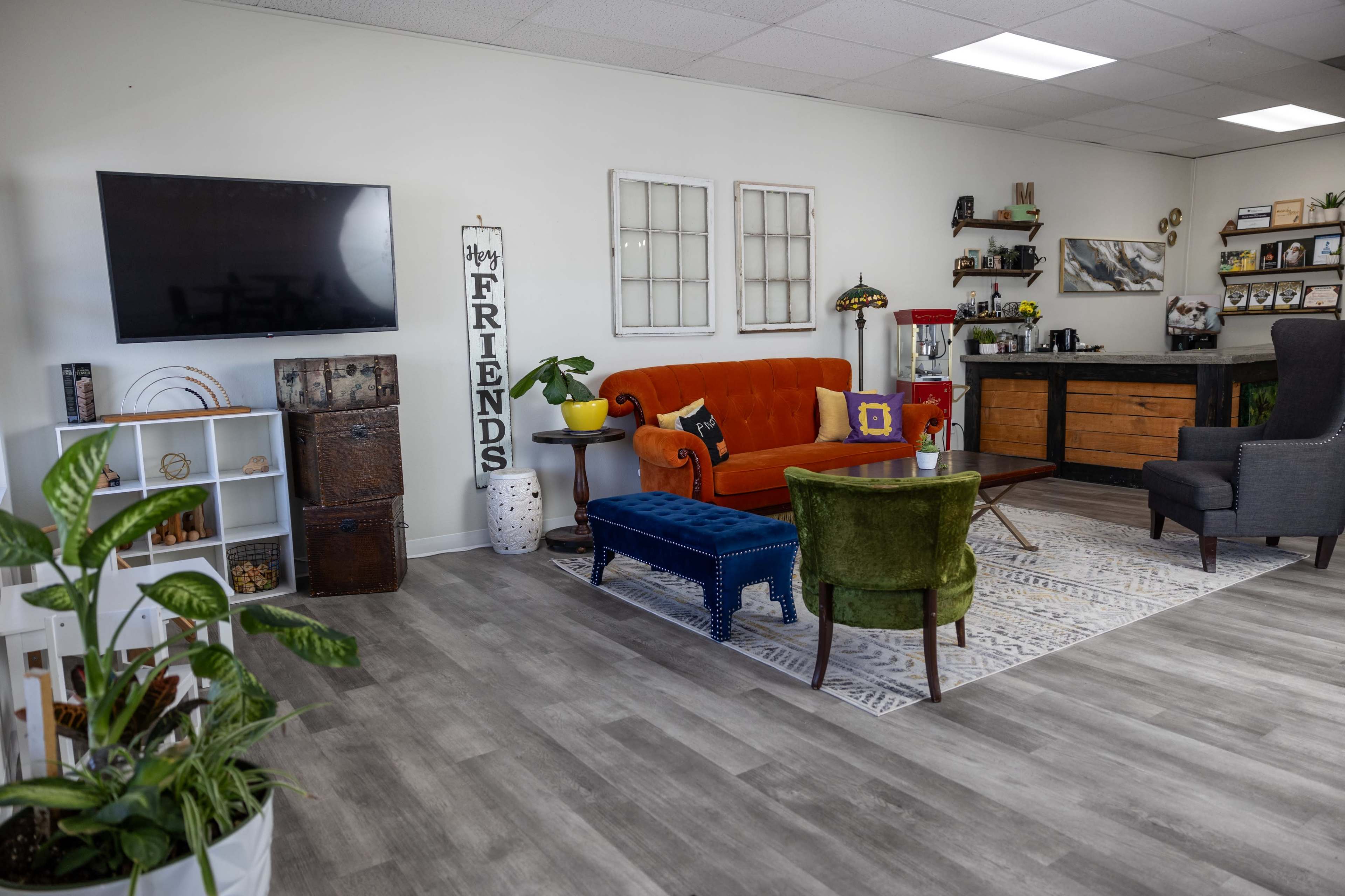 A cozy, modern living space with an orange sofa, green armchair, and a wooden coffee table, complemented by plants and decorative items on the walls and shelves.