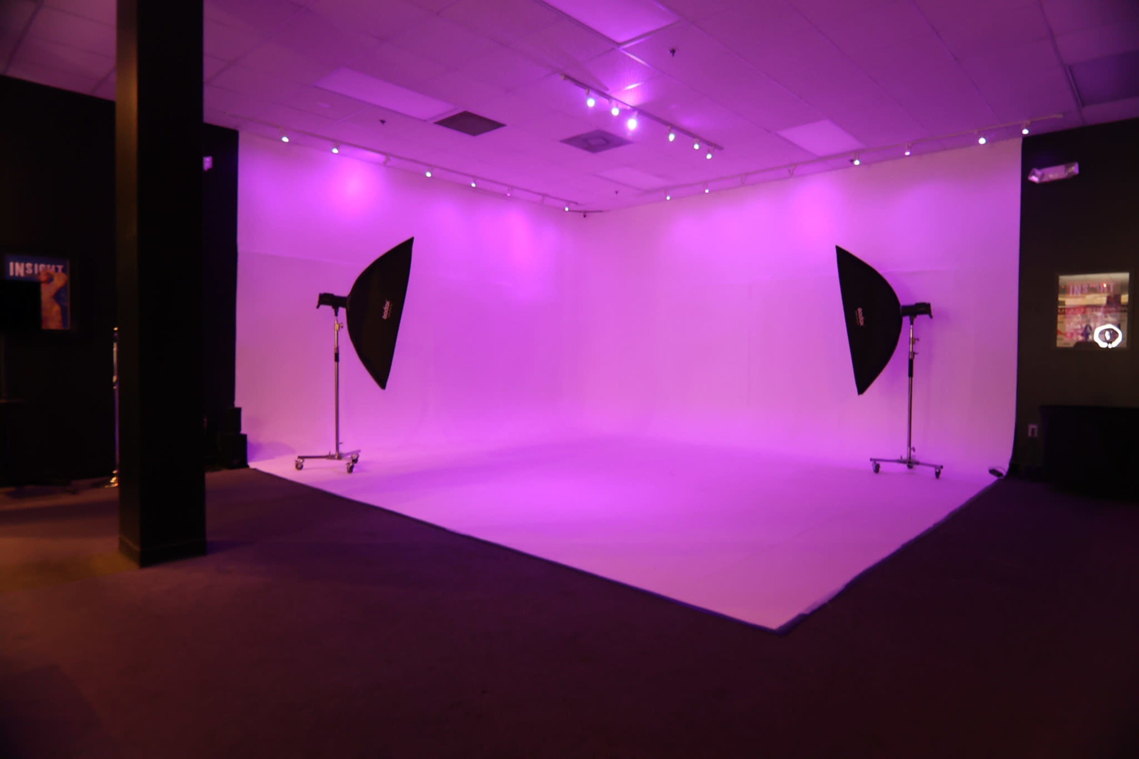 A photography studio features a brightly lit, purple backdrop with two large softboxes positioned on either side.