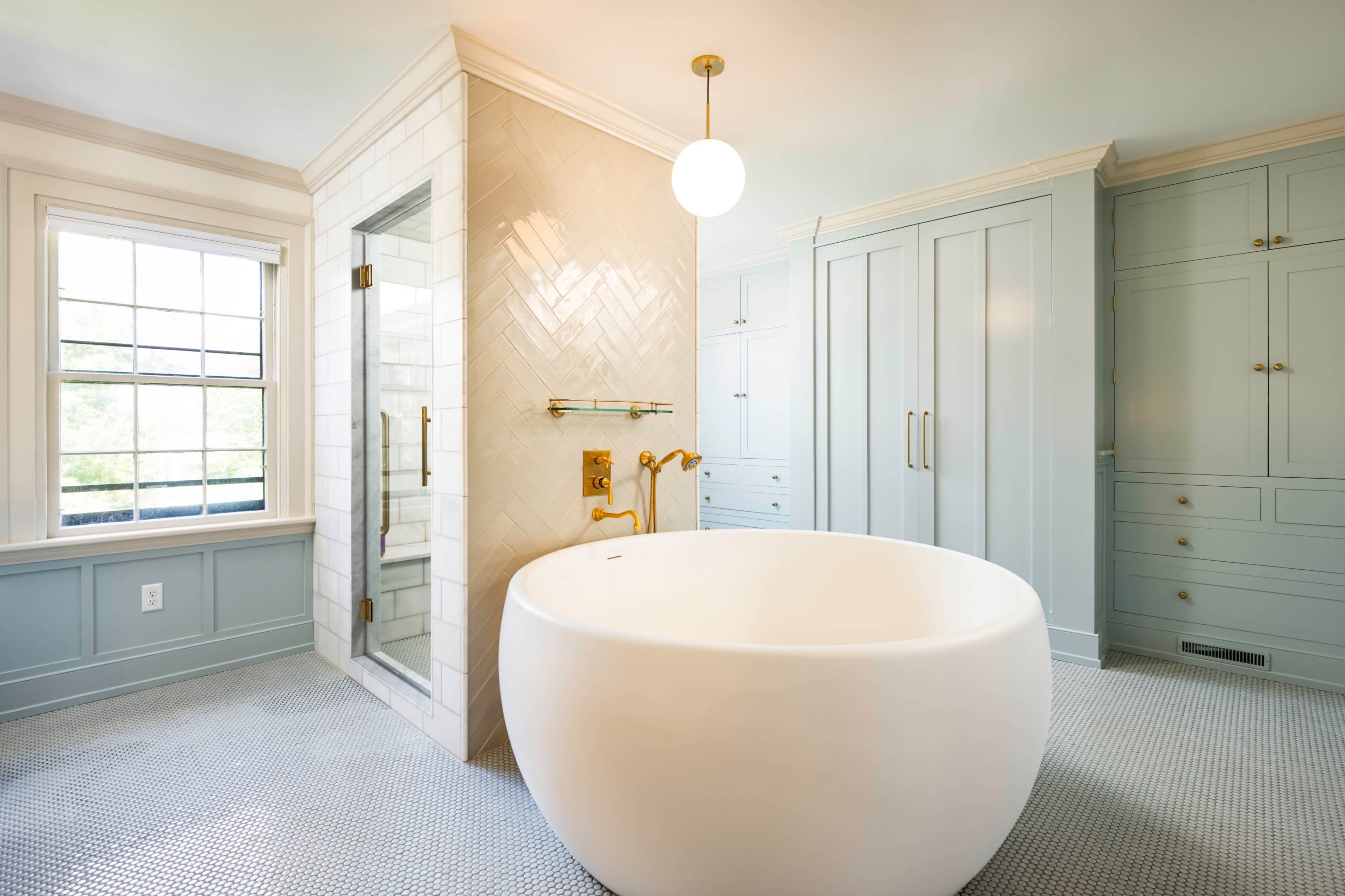 A modern bathroom featuring a freestanding oval bathtub, a glass shower enclosure, and cabinetry with a light blue finish.