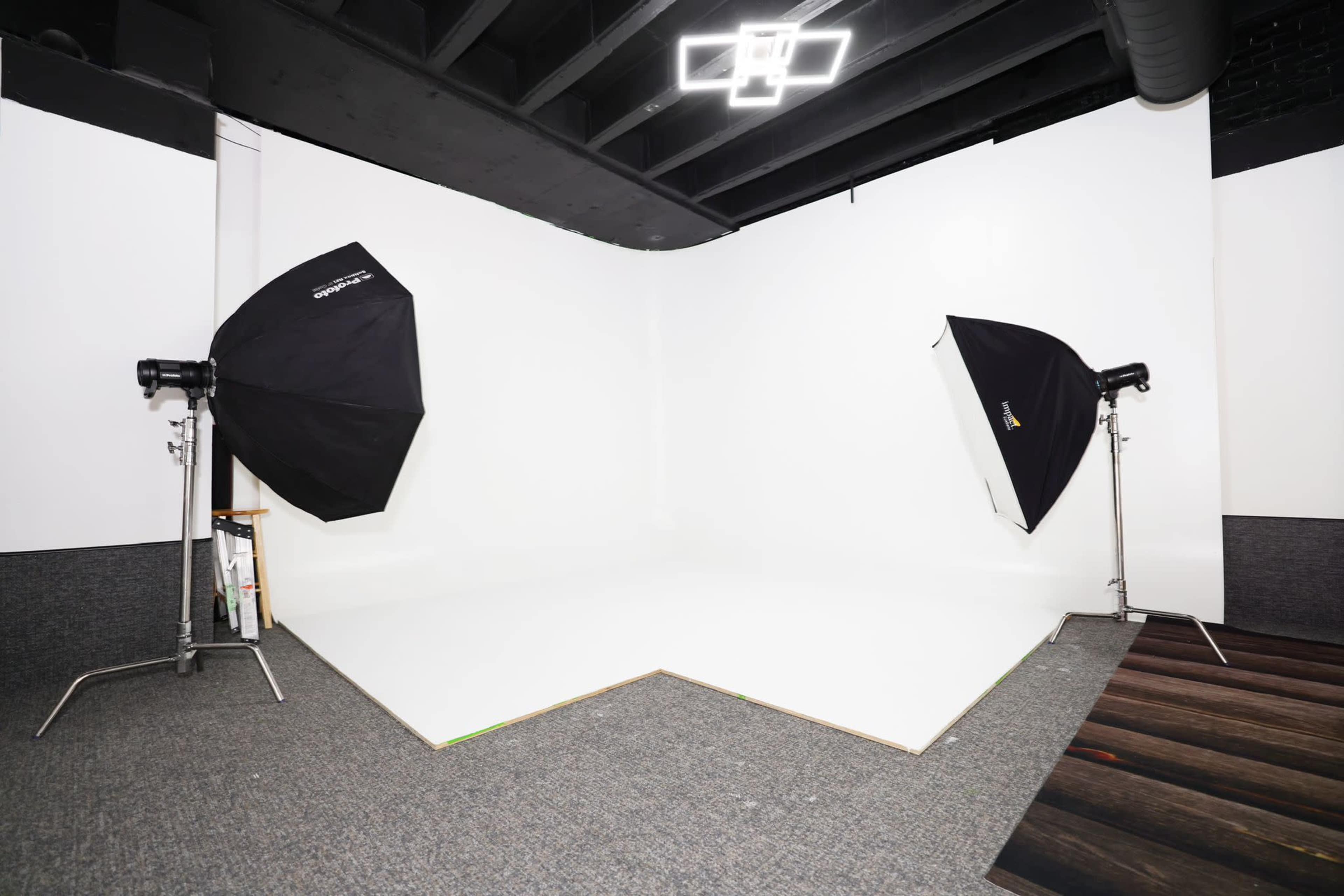 A photography studio with a white backdrop, two softbox light setups, and a carpeted floor.