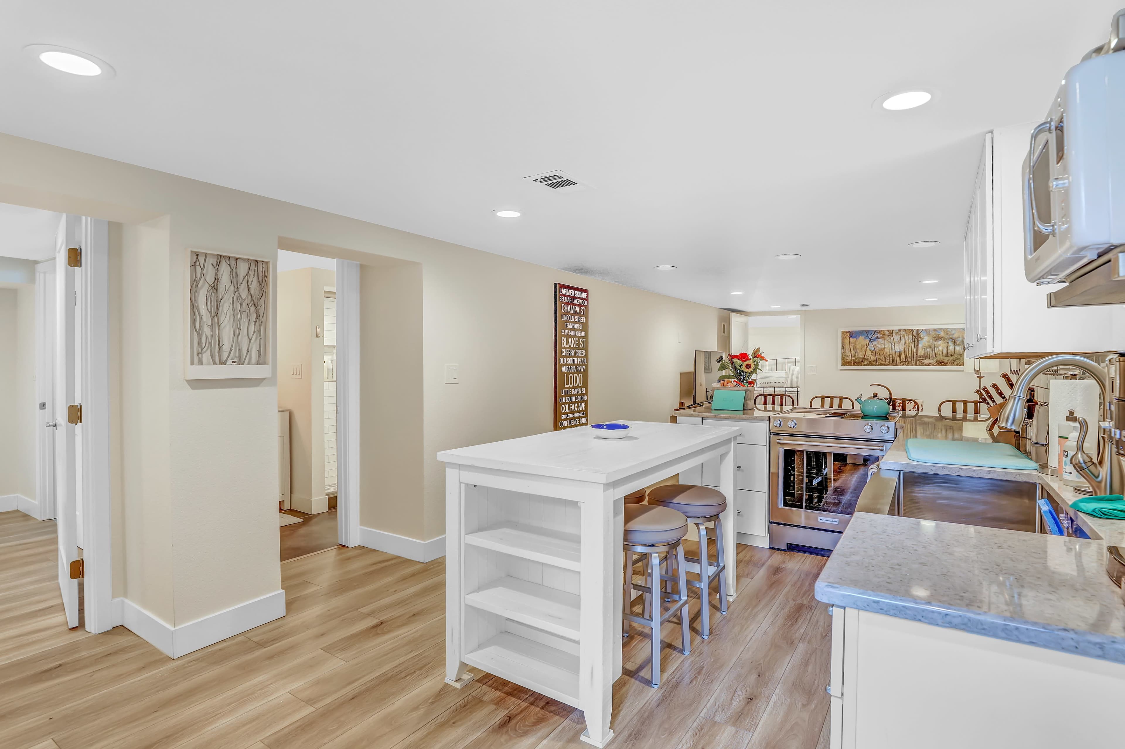 The image shows a modern kitchen with light-colored cabinetry, a central island with seating, and stainless steel appliances.