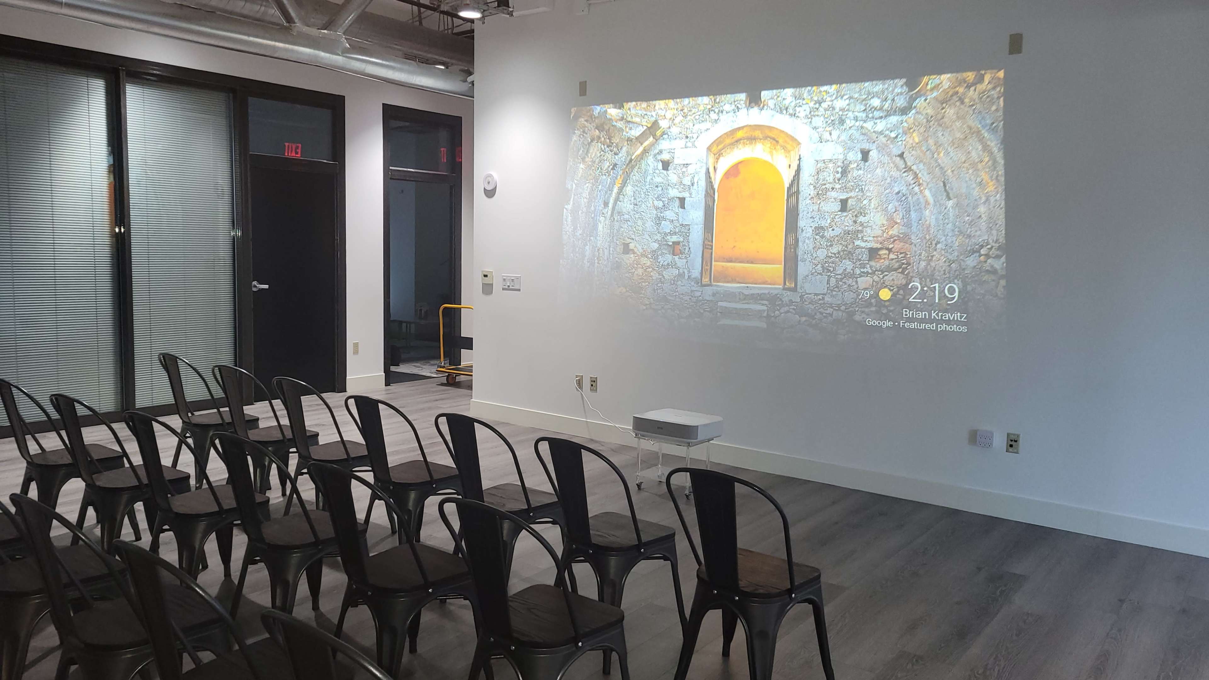 A minimalist room with rows of metal chairs facing a wall projecting an image of a stone archway.