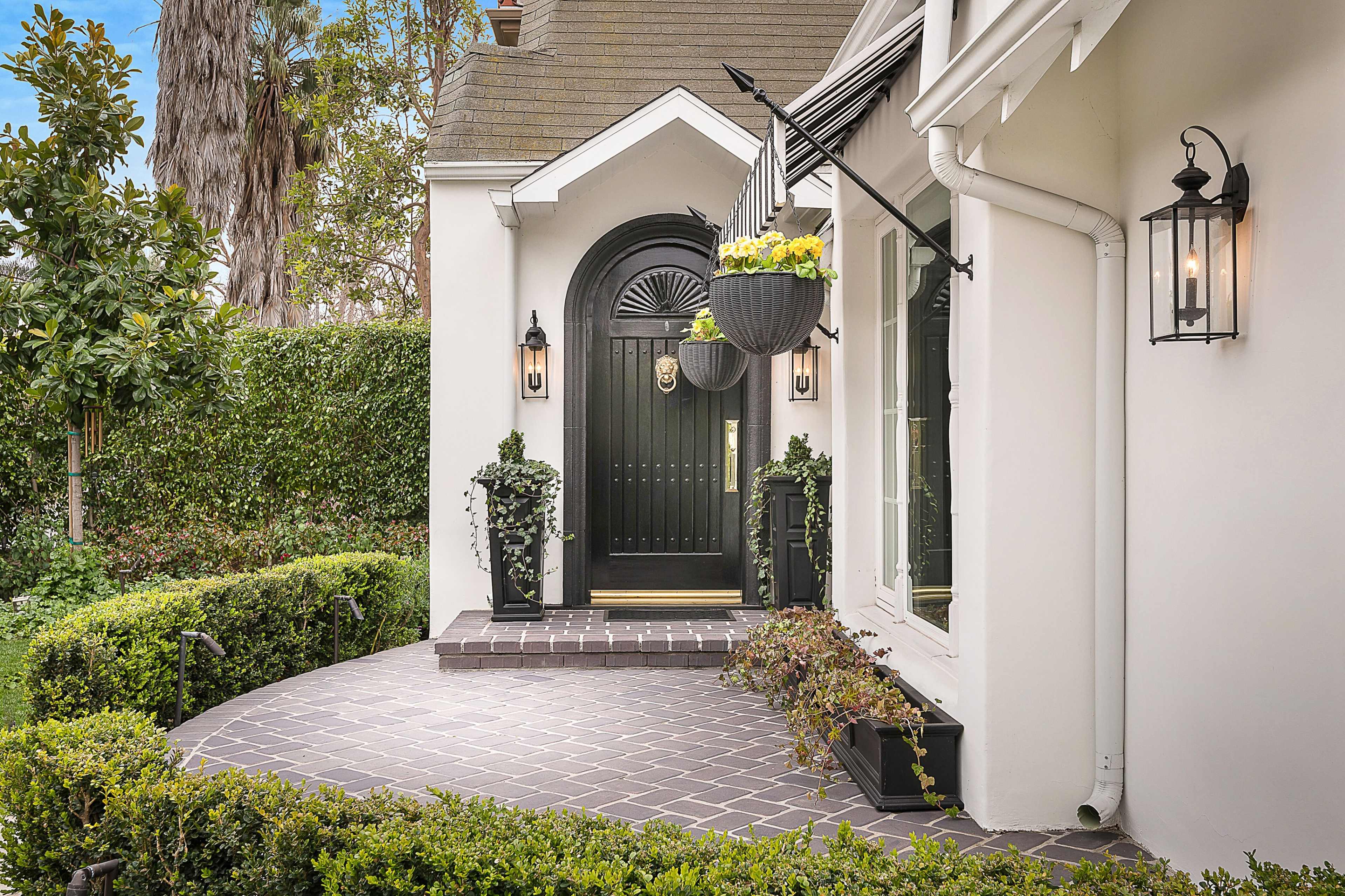A charming entrance with a black front door, decorative plants in planters, and a stone pathway lined with hedges.