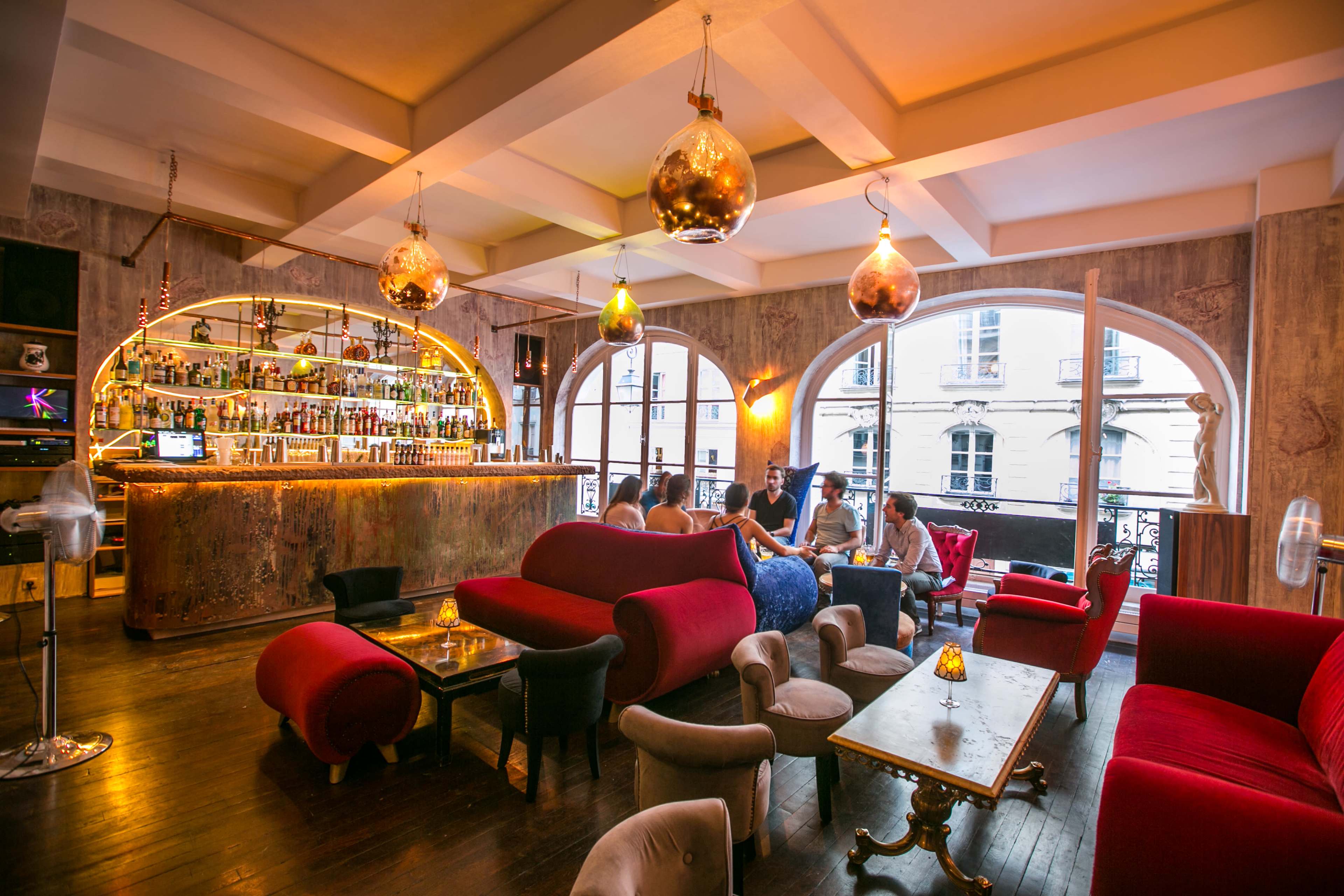 A stylish bar interior with a curved bar, plush red couches, and decorative pendant lighting.