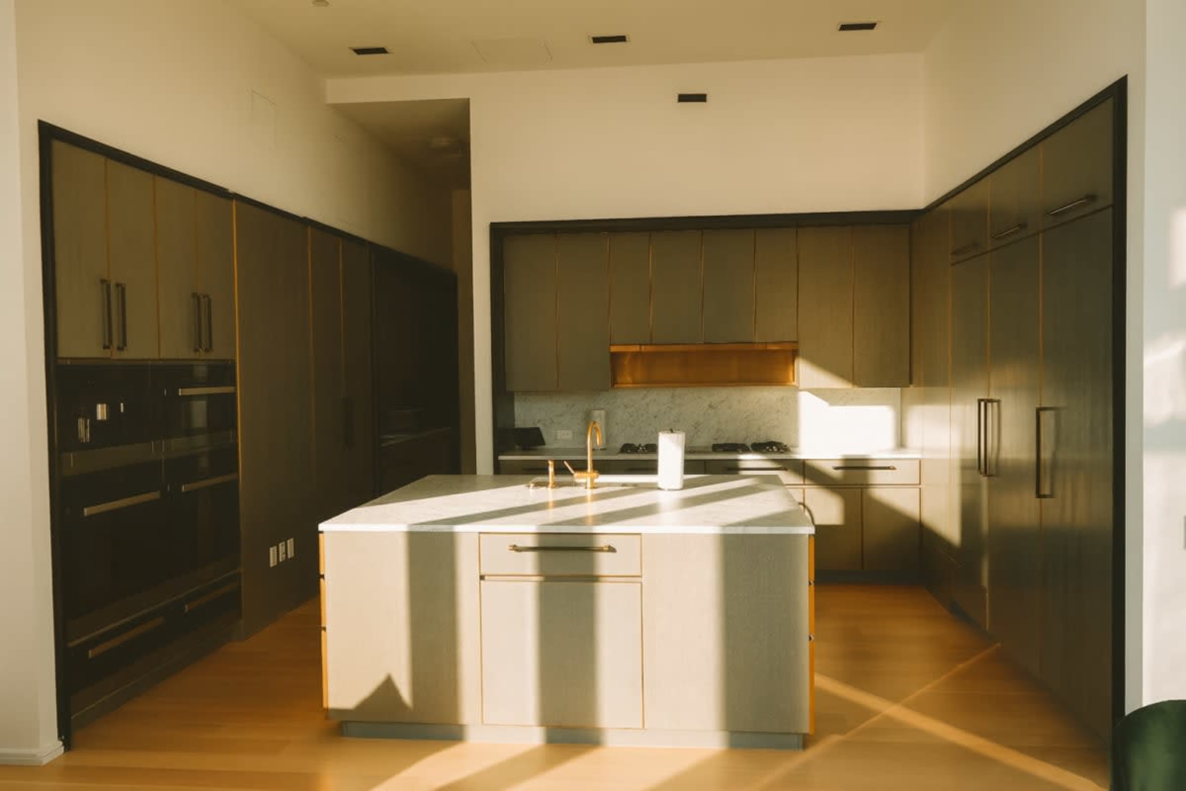 The image shows a modern kitchen with dark cabinetry, a central island, and natural light streaming through a window.
