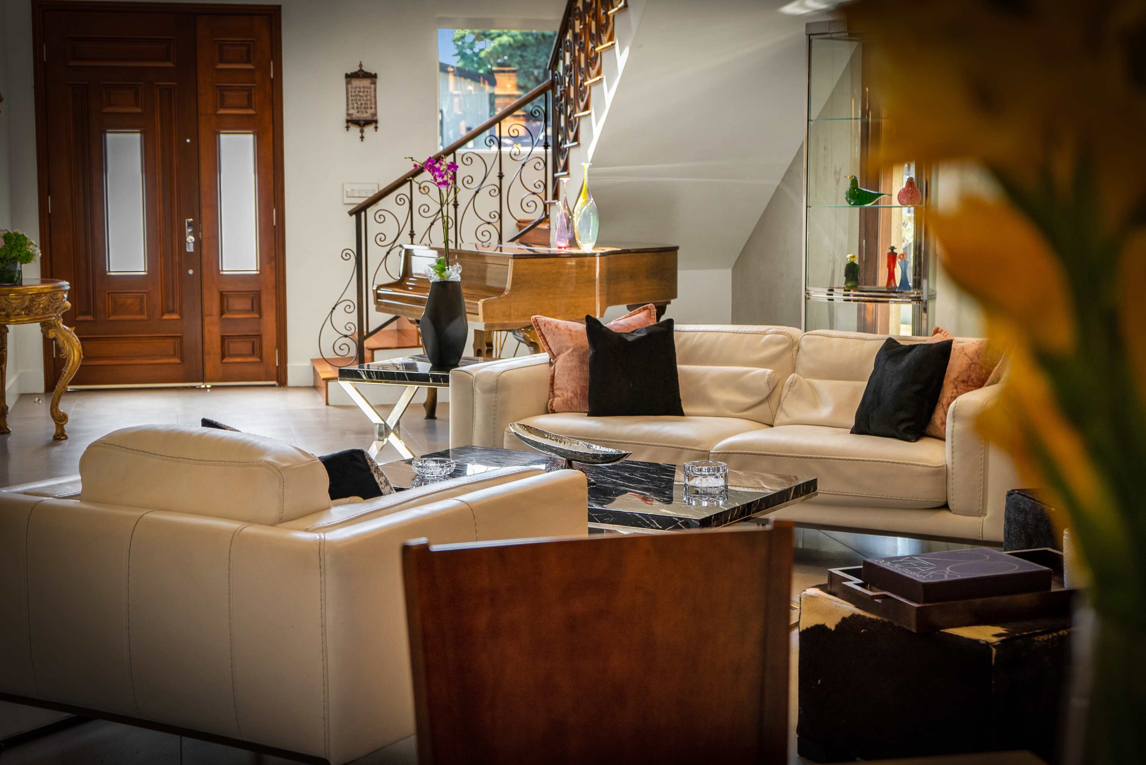 A modern living room with a cream-colored leather sectional, a black coffee table, and a grand piano in the background near a staircase.