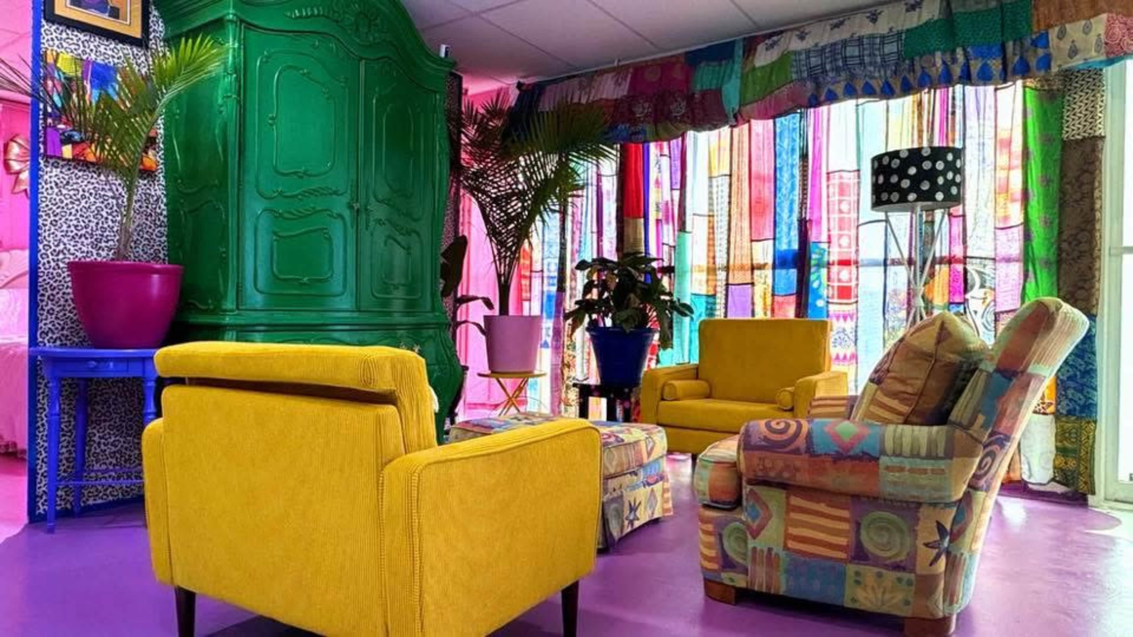 The image shows a brightly colored room with yellow and patterned sofas, a green cabinet, and decorative curtains made of various fabrics.