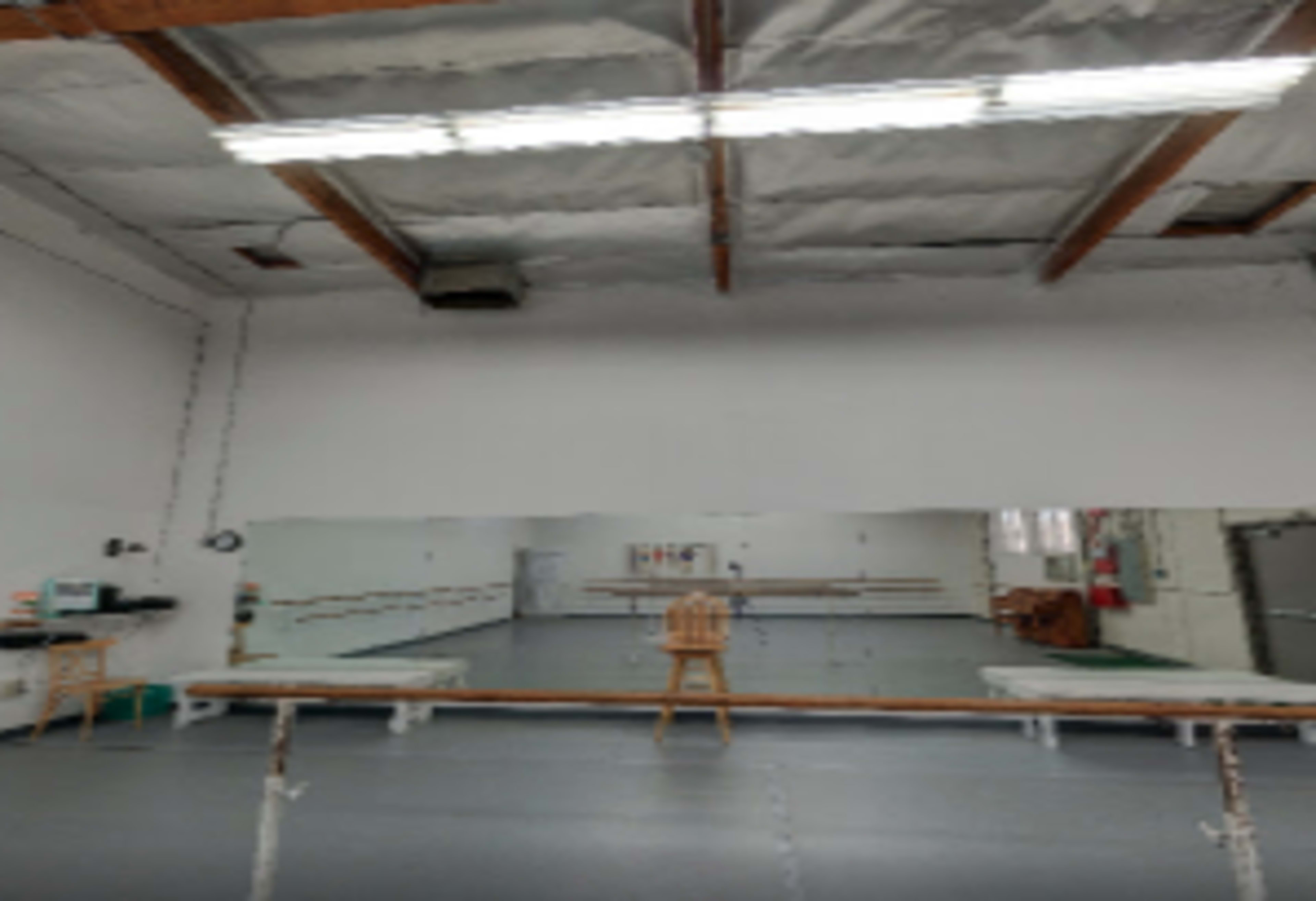 An empty dance studio with mirrors, a wooden barre along the wall, and overhead lighting.