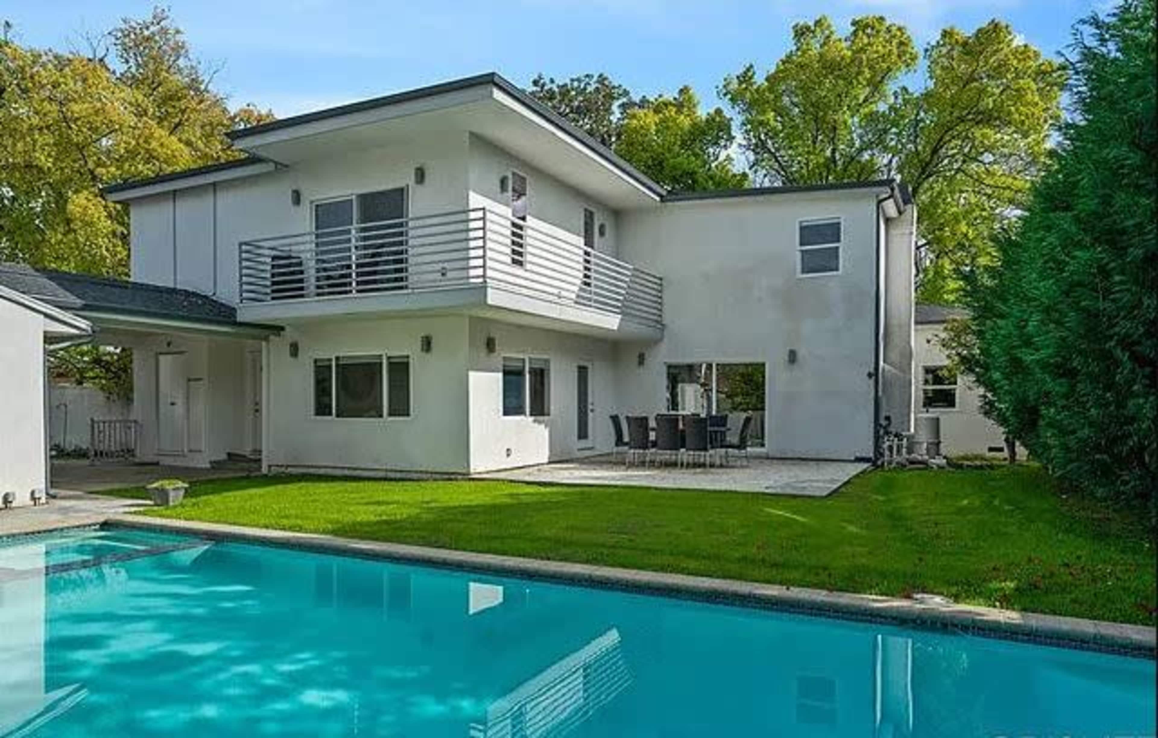 A modern two-story house with a swimming pool and a patio area surrounded by greenery.