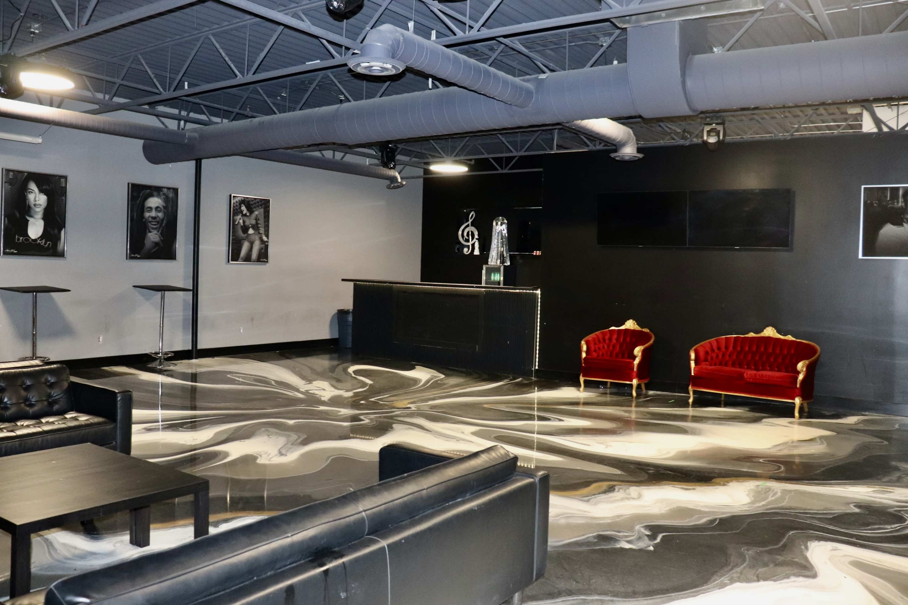 The image shows a modern interior space with a polished marble floor, black walls, a reception area with a counter, and two red velvet sofas.