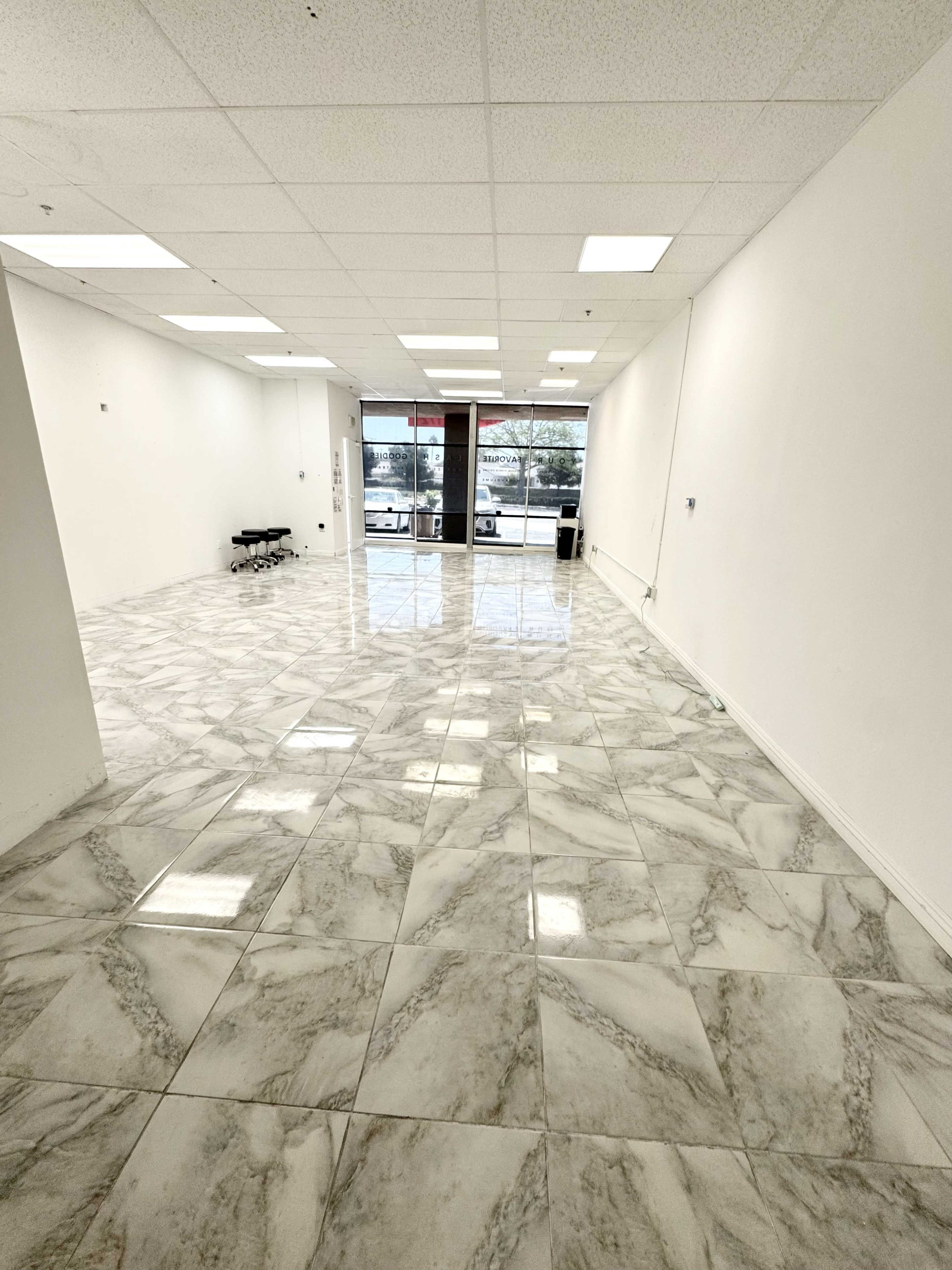 The image shows a vacant interior space with glossy marble floors, white walls, and large windows letting in natural light.