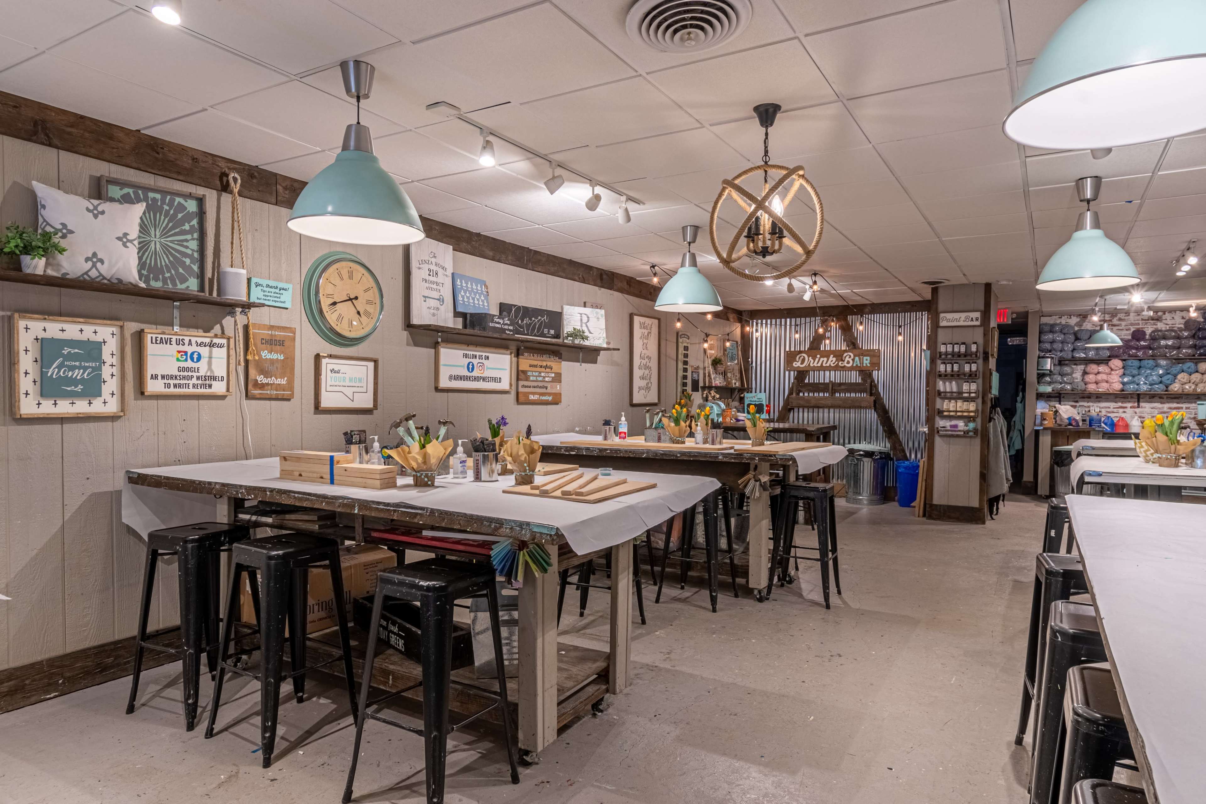 An art studio with multiple work tables, pendant lighting, and supplies organized for creative activities.