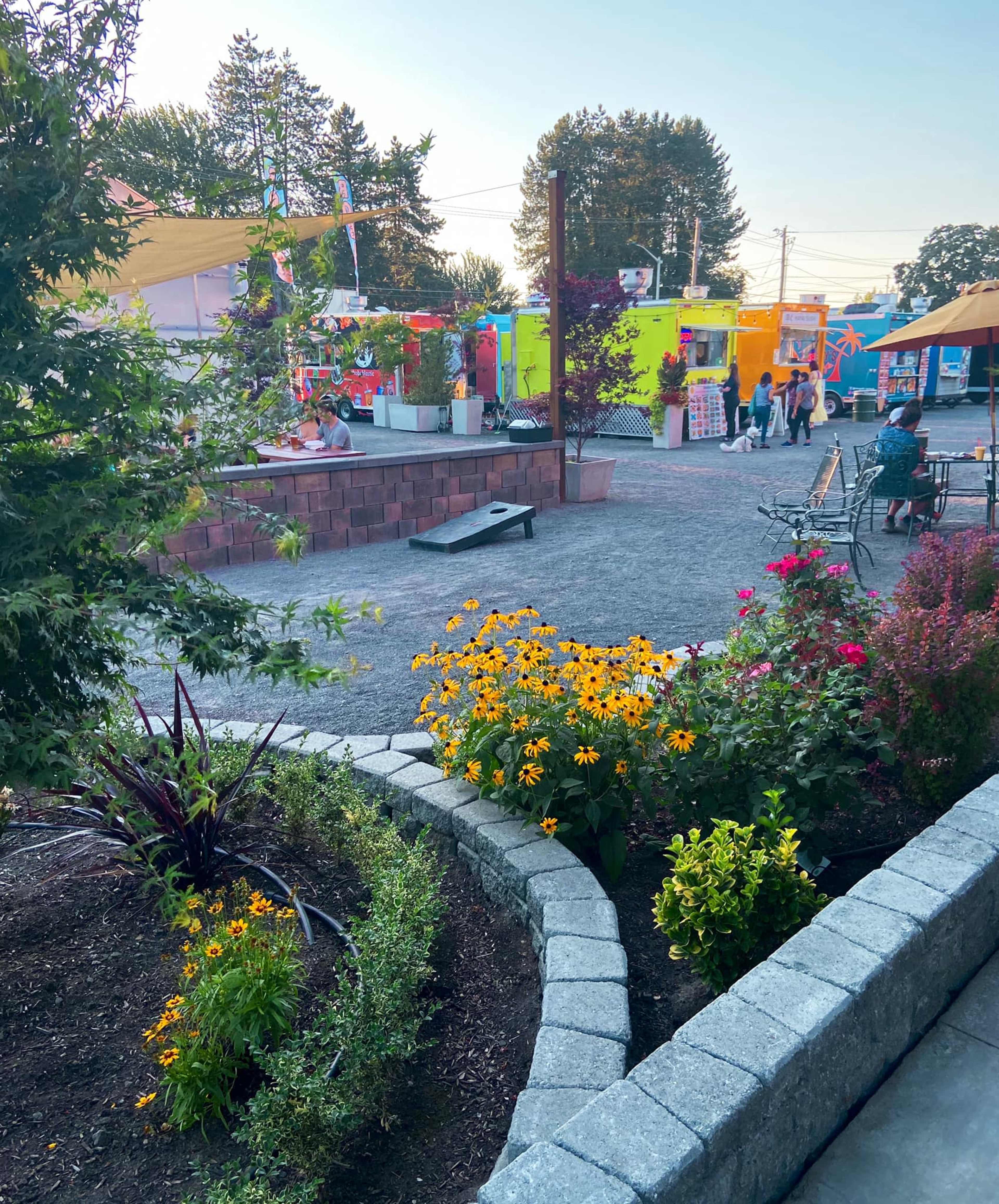 A vibrant food truck area is surrounded by a landscaped garden with colorful flowers and seating spaces for visitors.