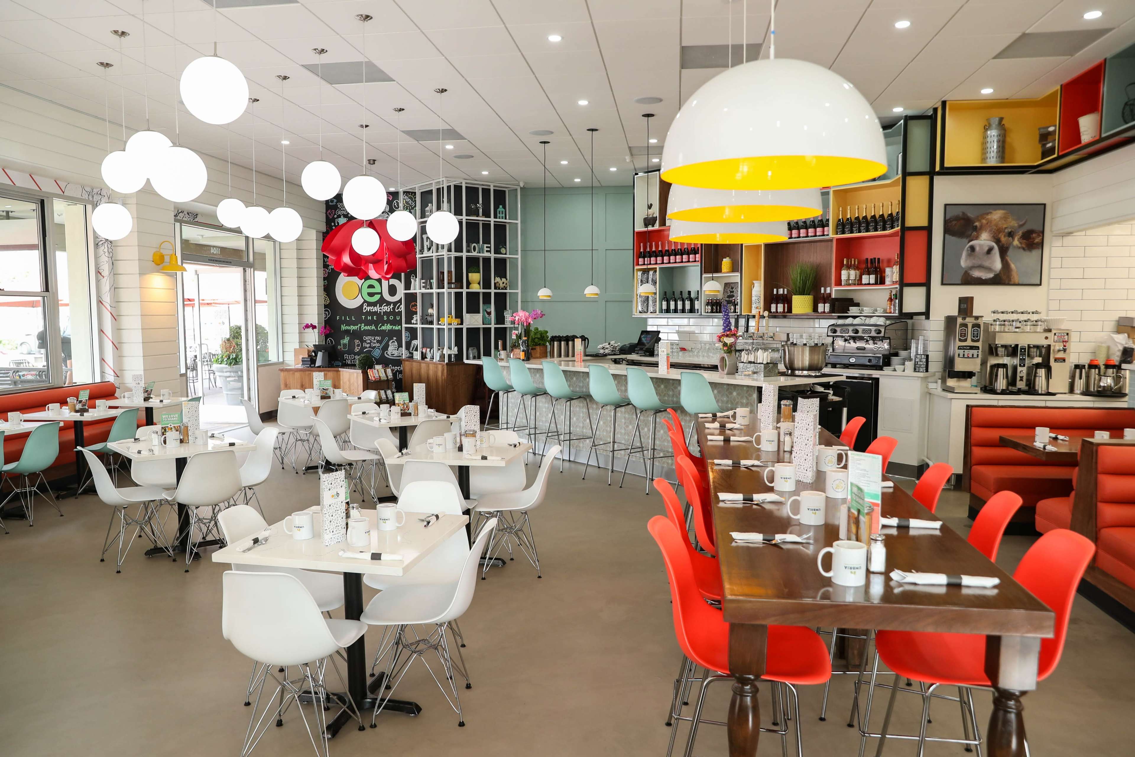 A modern restaurant interior with colorful furniture, round pendant lights, and a bar area in the background.