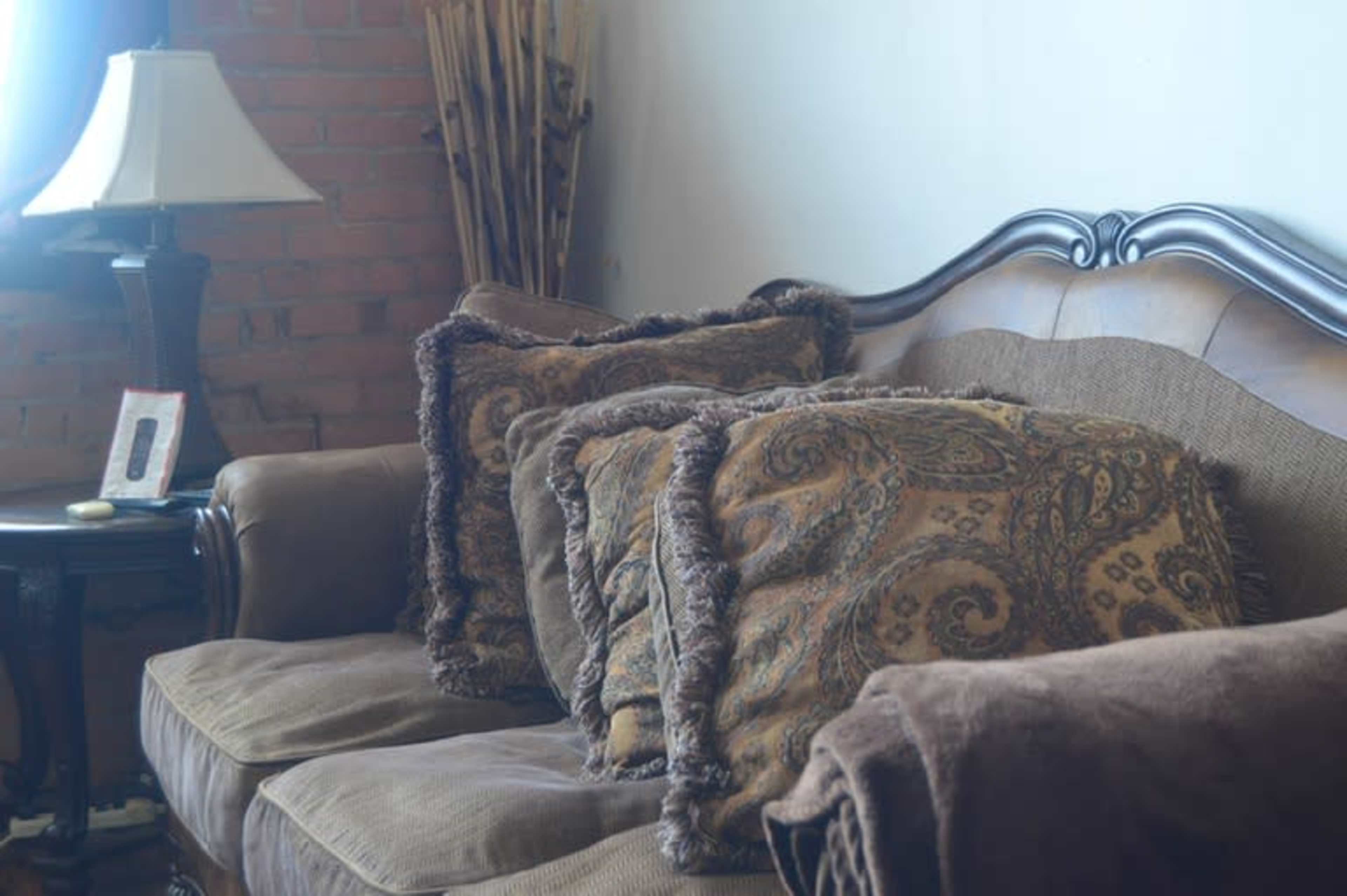 A sofa with decorative pillows and a lamp on a side table in a well-lit living room.