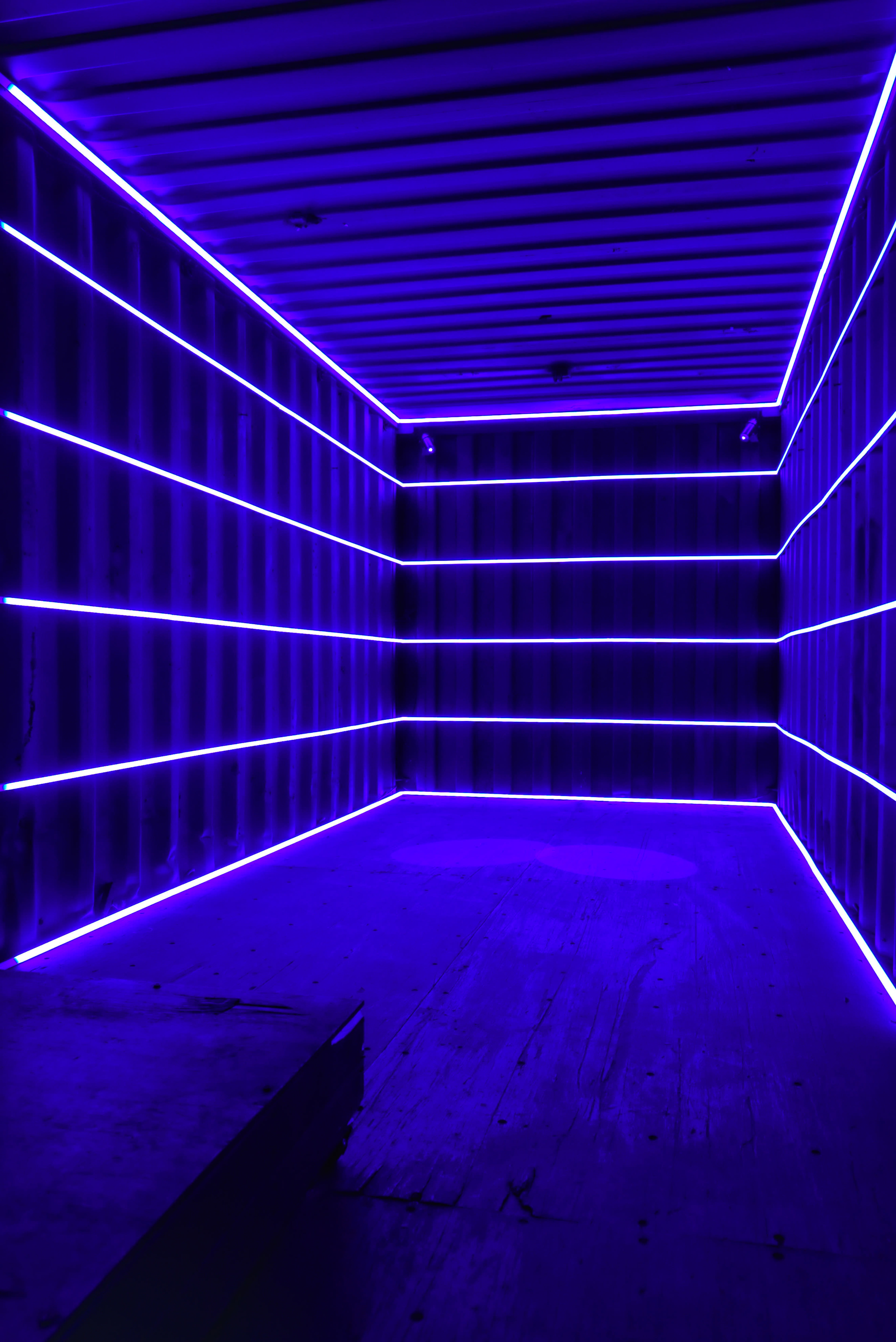 The image shows the interior of a shipping container illuminated by bright purple neon lights along the walls.