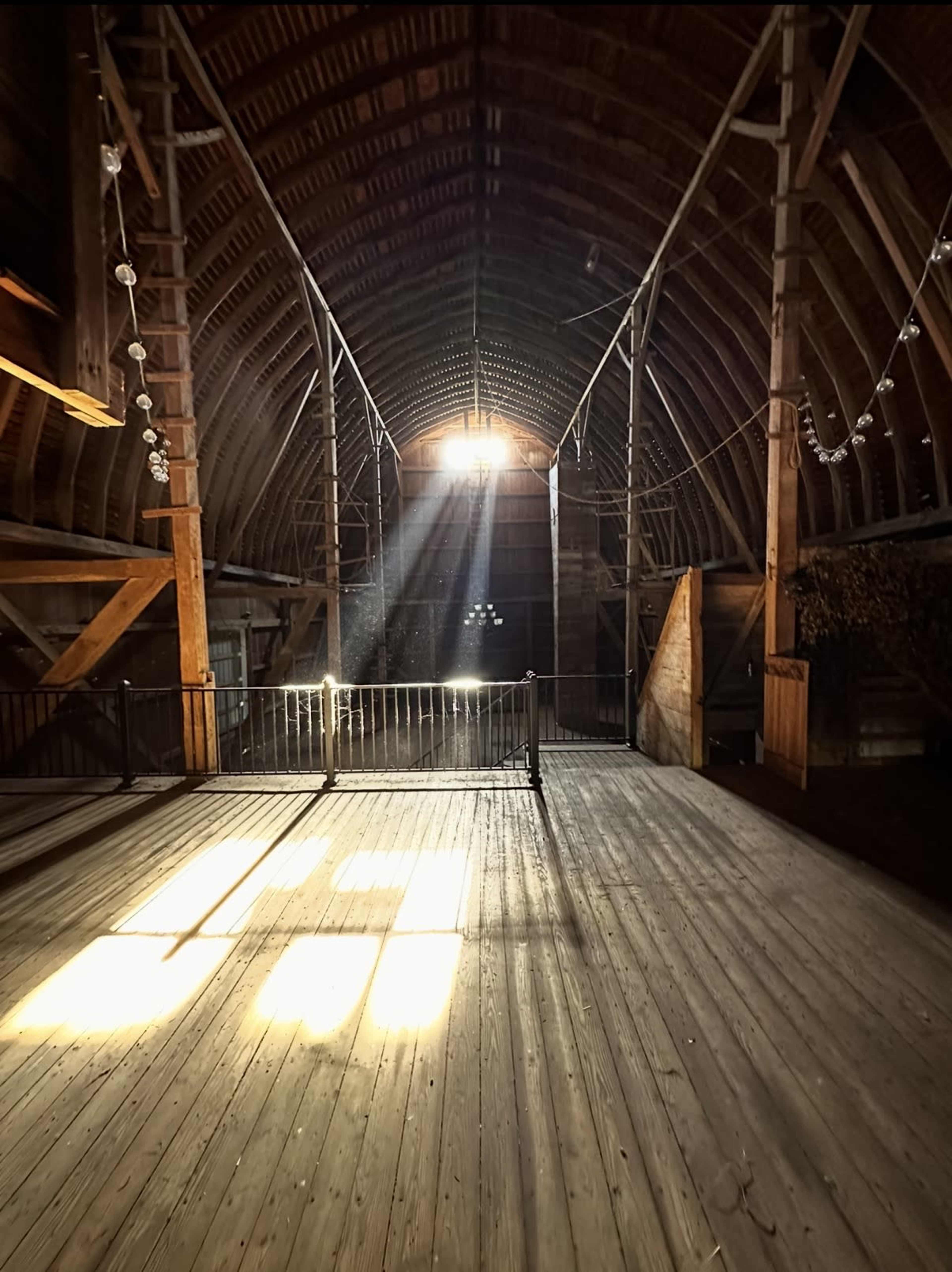 A sunbeam streams through the openings at the top of a wooden barn, illuminating the empty wooden floor inside.