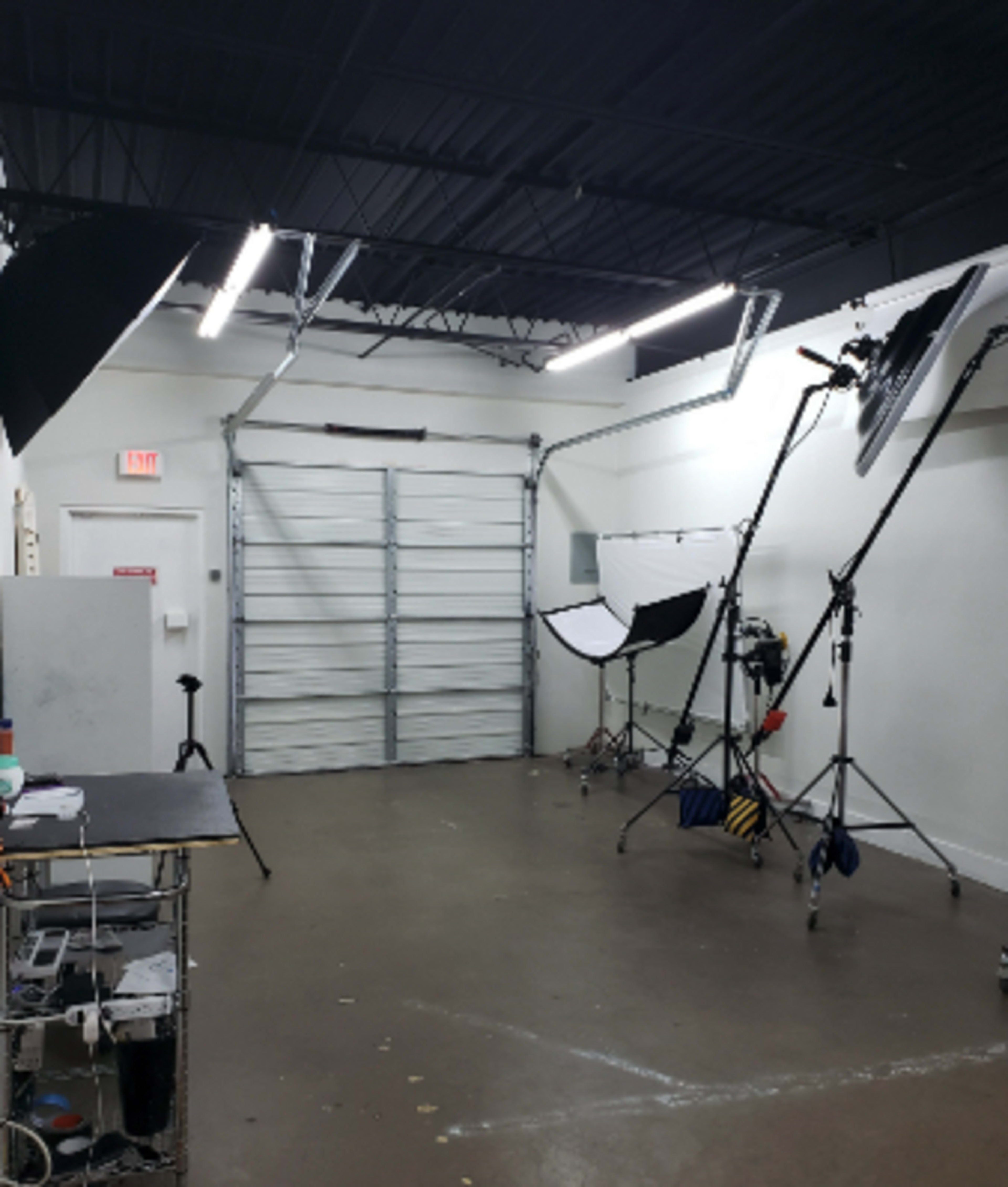 The image shows a photography studio with lighting setups, a table, and a large garage door.