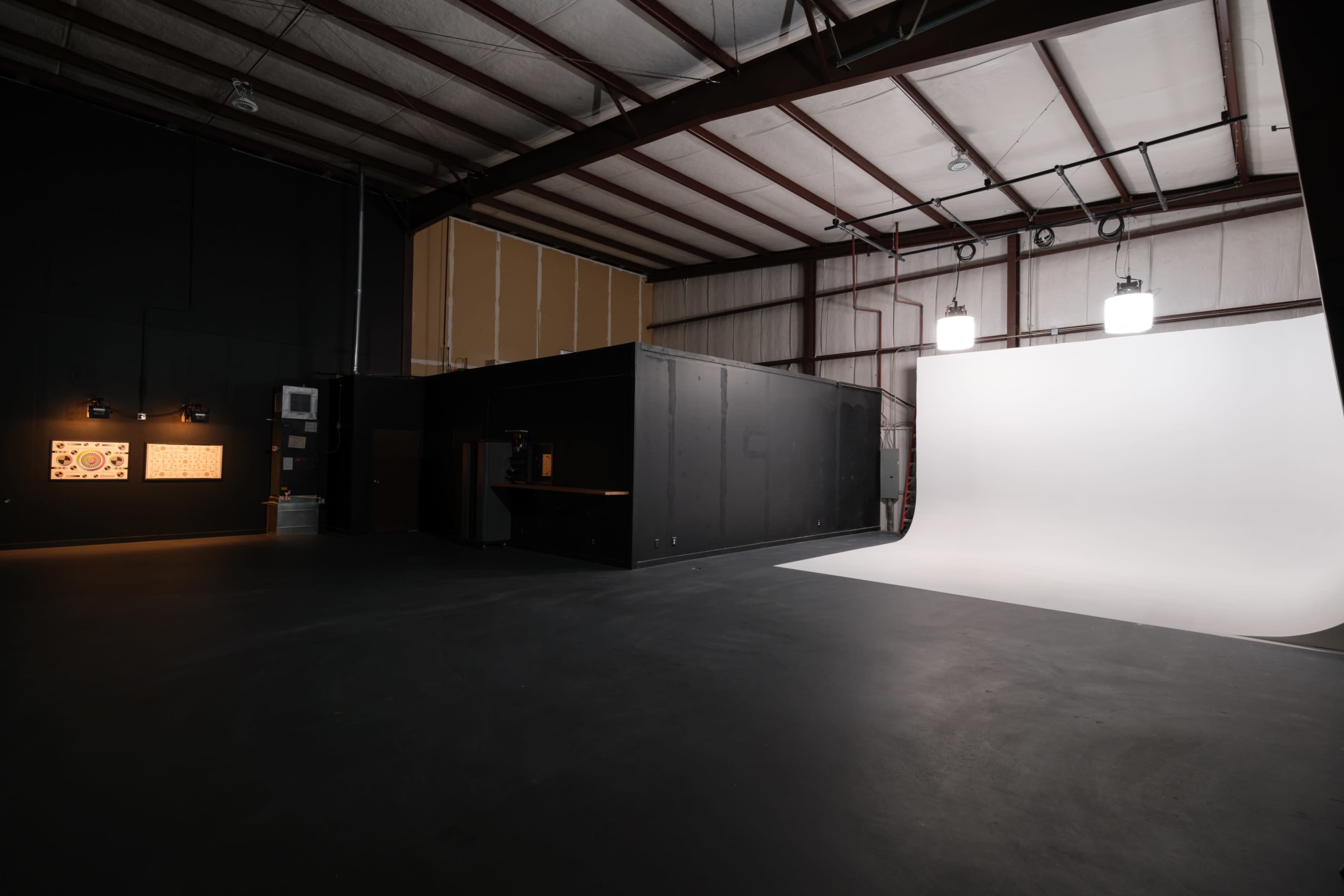 The image shows a spacious studio with a white backdrop on one side and a dark section with wall-mounted displays on the other.