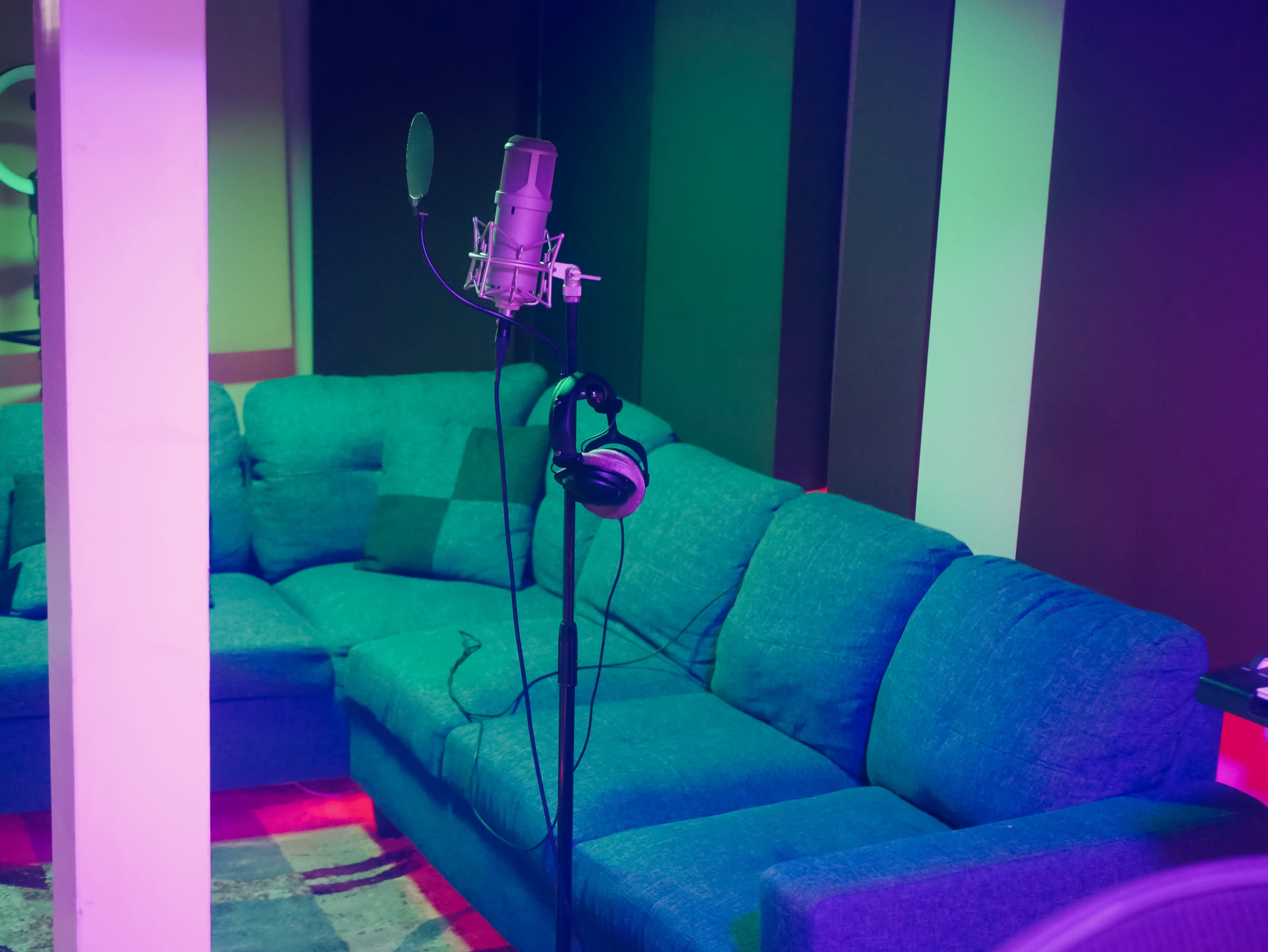 A microphone on a stand is positioned near a teal couch in a dimly lit recording studio.