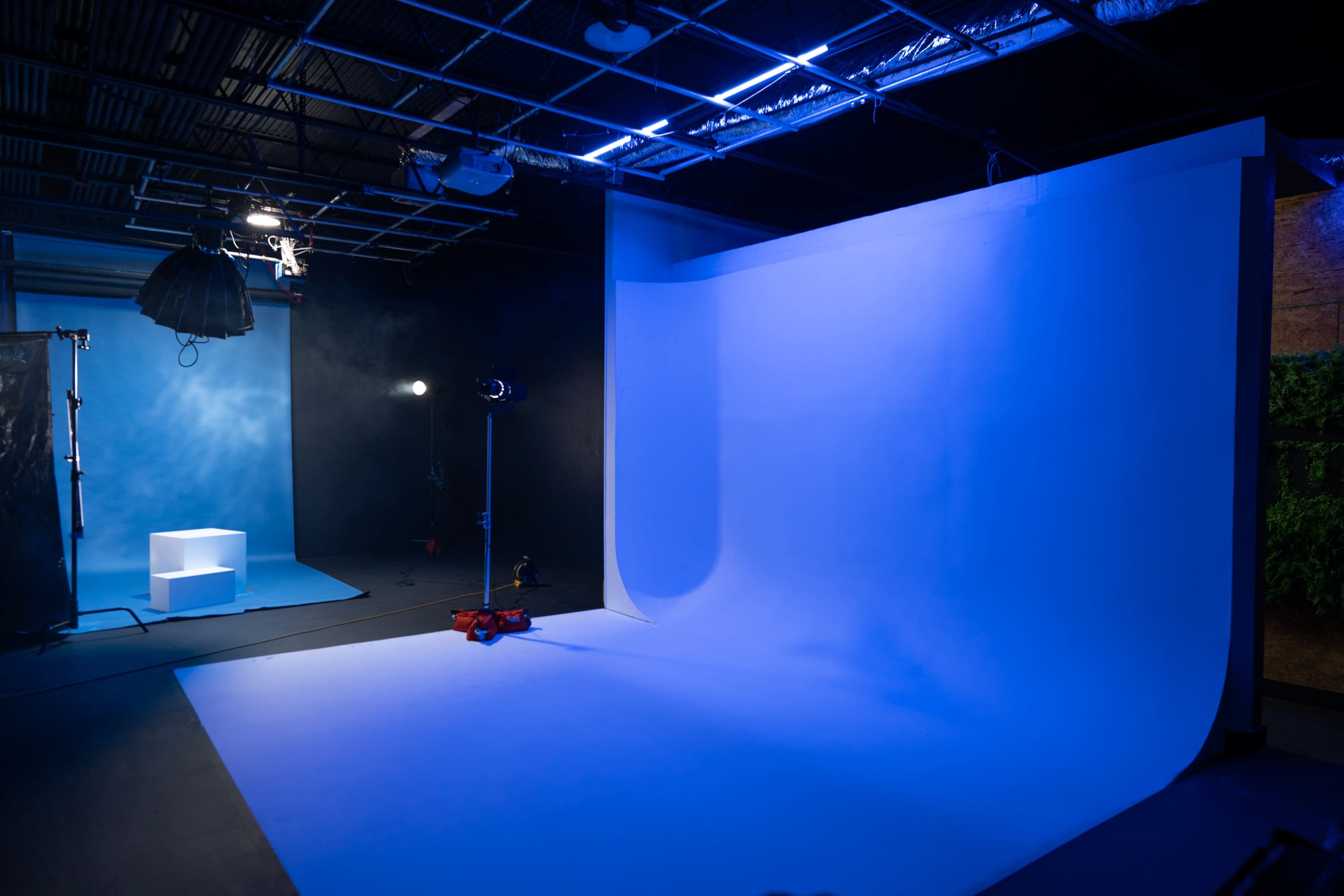 A photography studio with a blue backdrop, a light setup on the left, and a small white platform in the background.