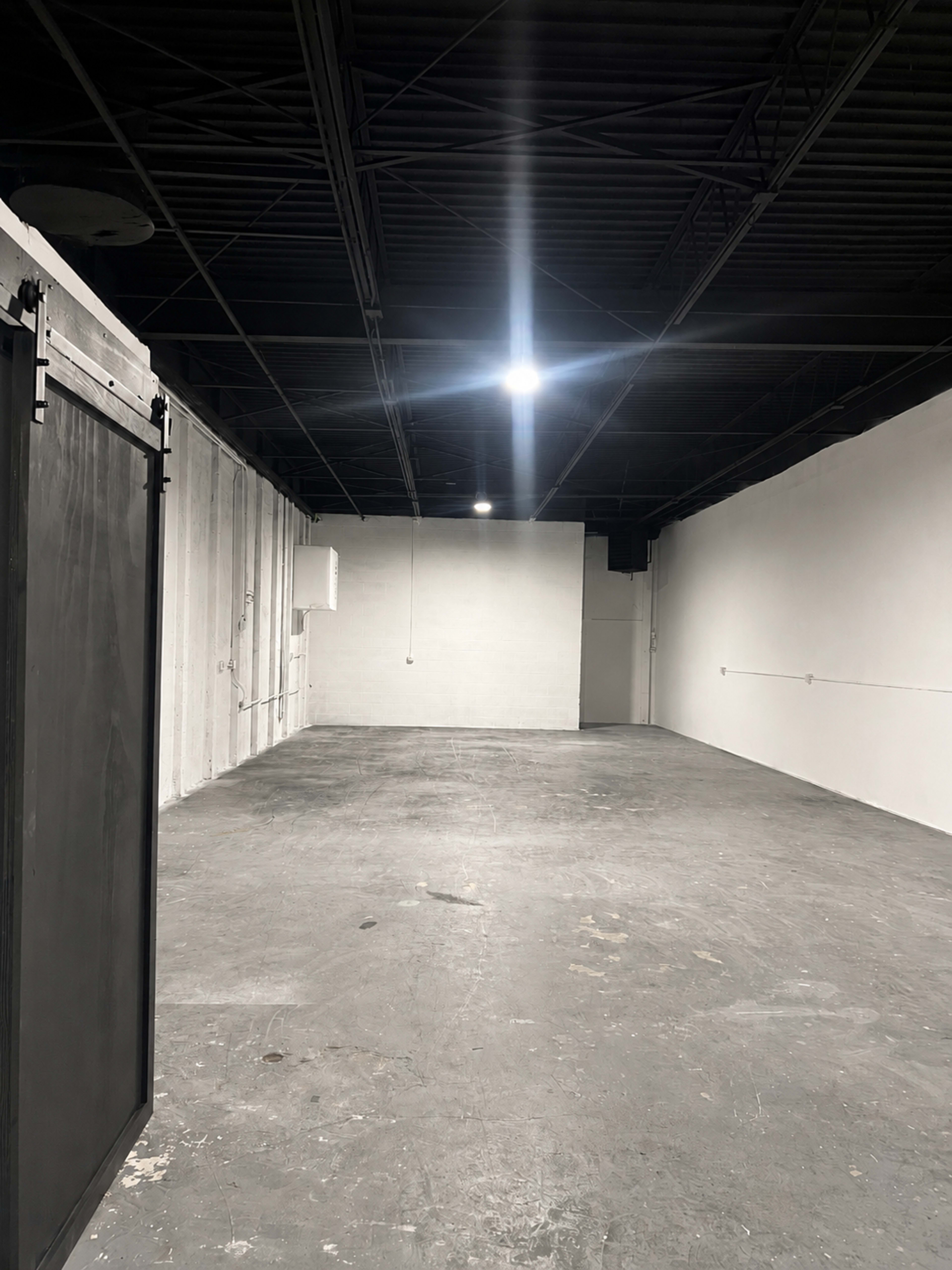The image shows a spacious, empty room with concrete flooring and white walls under bright overhead lighting.