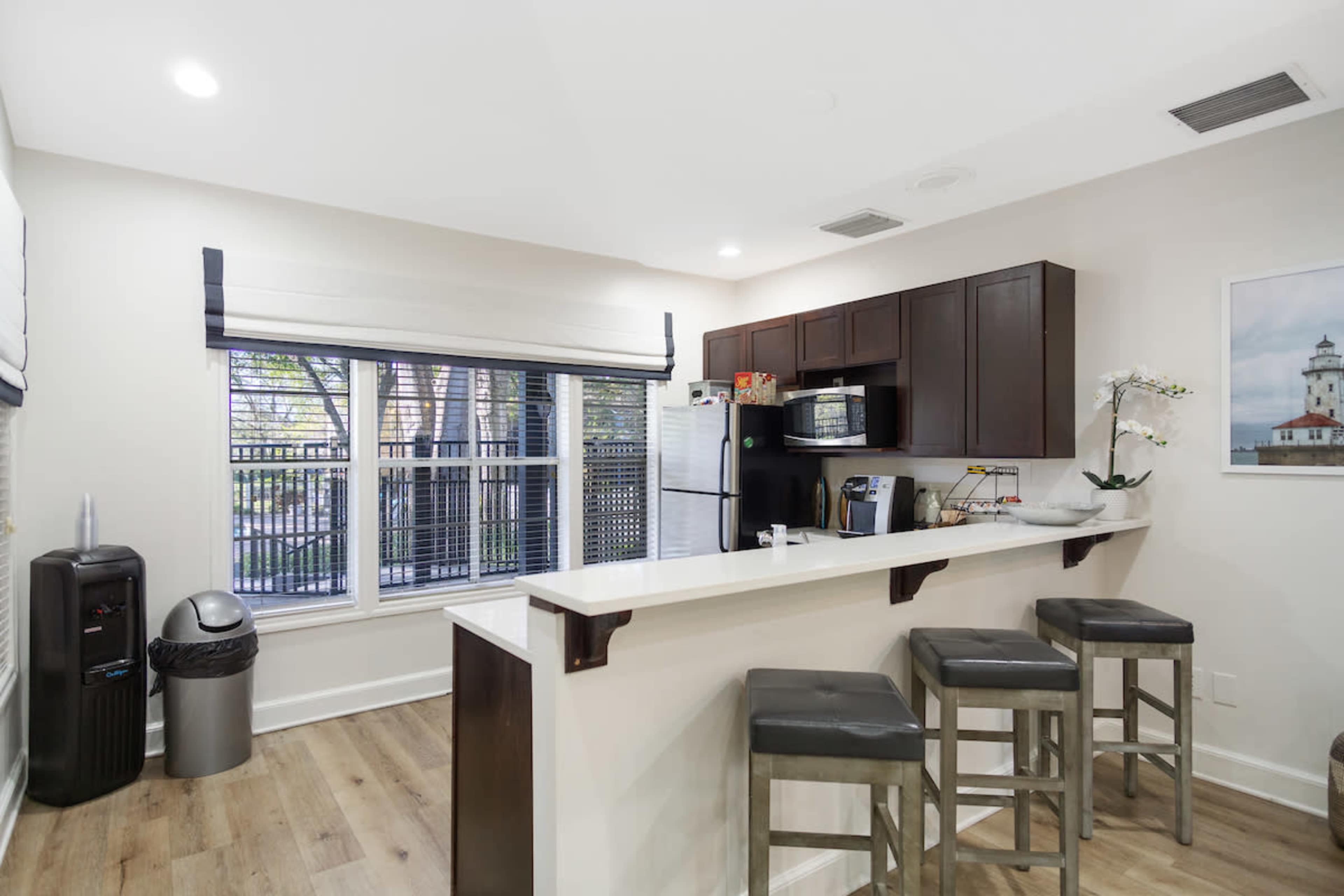 A modern kitchen with dark cabinetry, a breakfast bar with stools, and large windows overlooking an outdoor area.