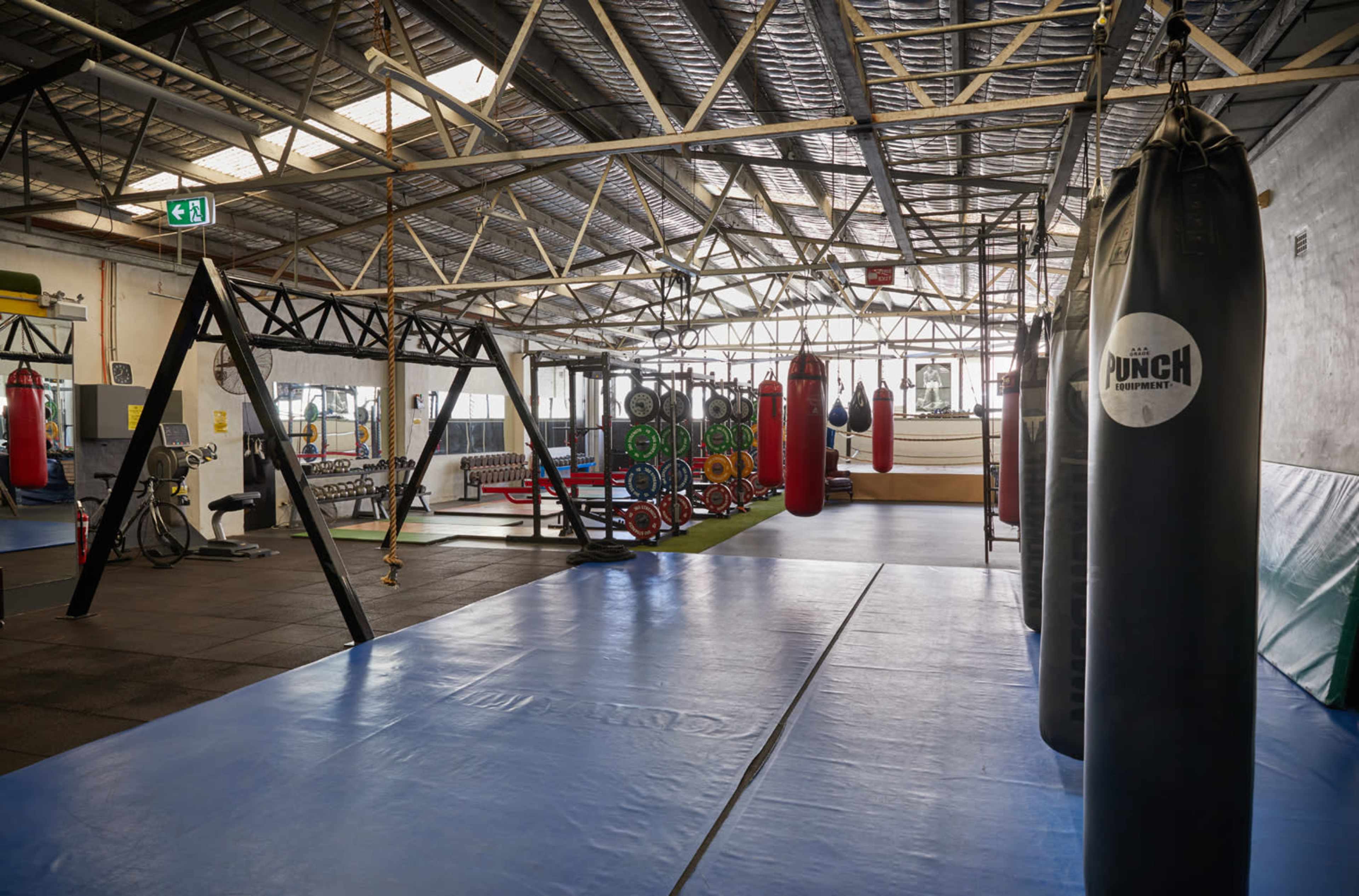 A well-equipped gym with punching bags, weights, and exercise mats set in a spacious, industrial-style facility.