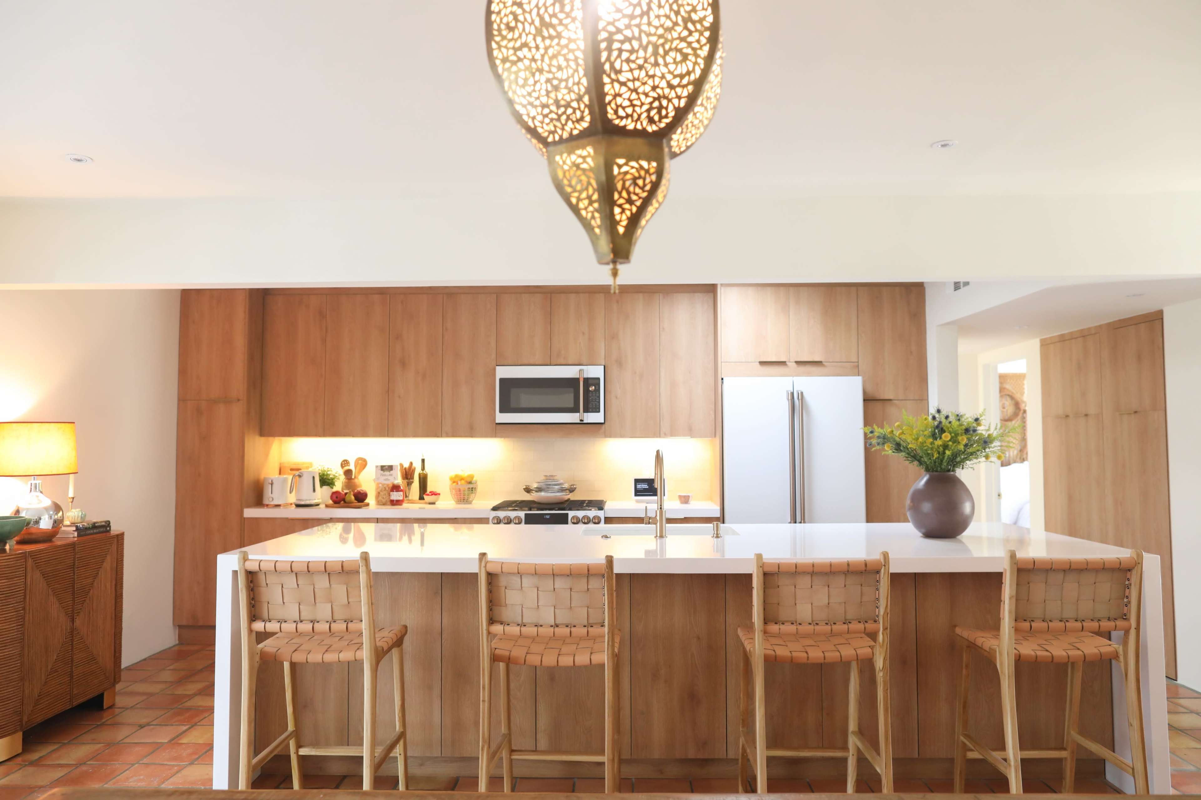 A modern kitchen with wooden cabinetry, a central island with seating, and a pendant light hanging above.