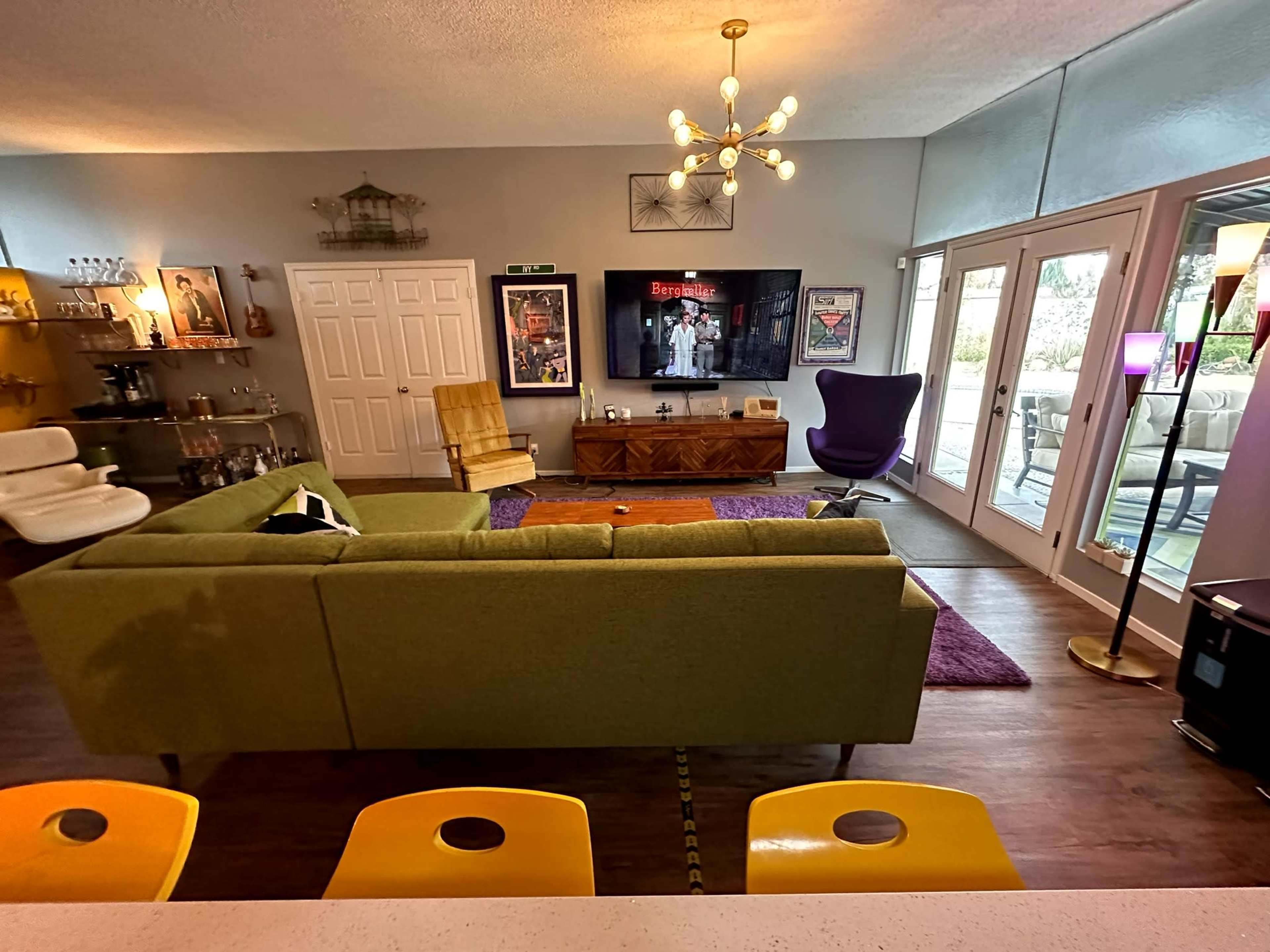 A modern living room with a green sectional sofa, a wooden entertainment unit, and large windows leading to a patio area.