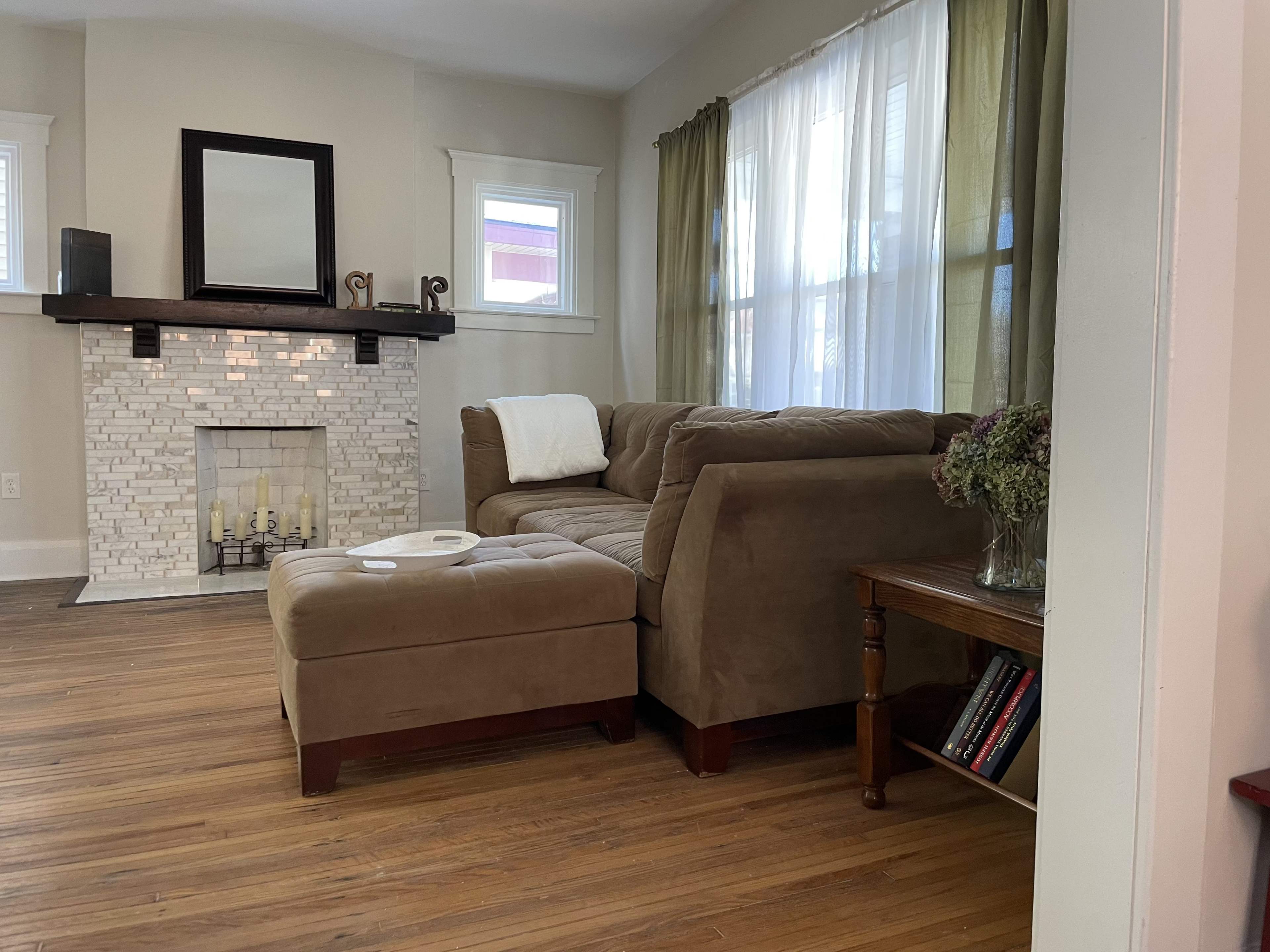 A living room with a brown sectional sofa, a stone fireplace, and a small wooden table with books beside it.