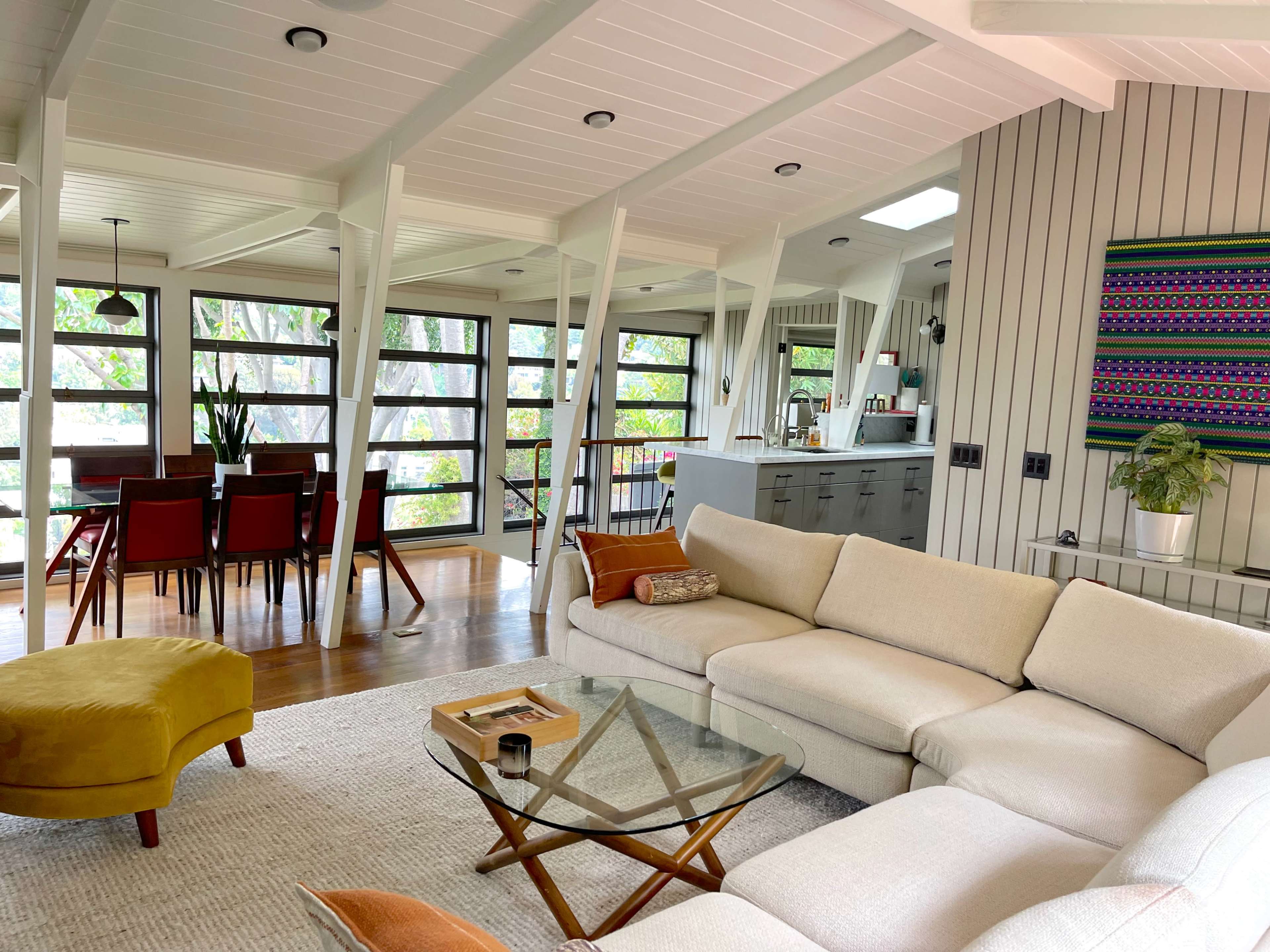 A modern living room with a sectional sofa, a glass coffee table, and a dining area visible in the background.