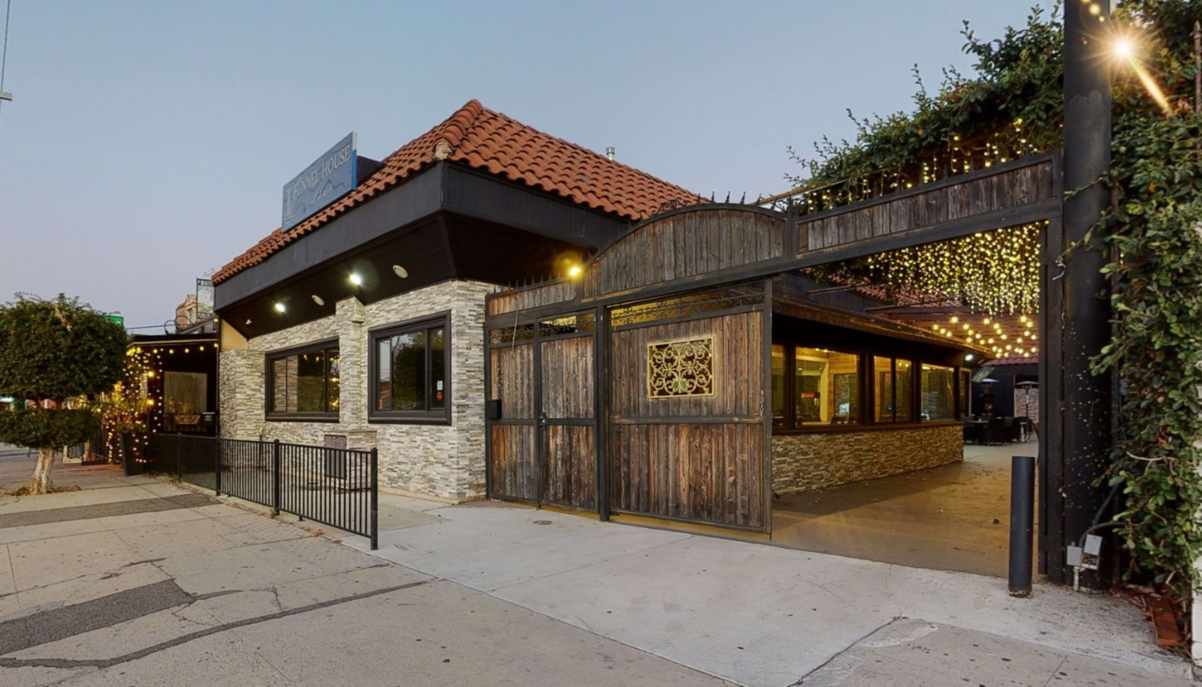 A restaurant with a stone and wood exterior is illuminated by string lights, featuring large windows and a tiled roof.