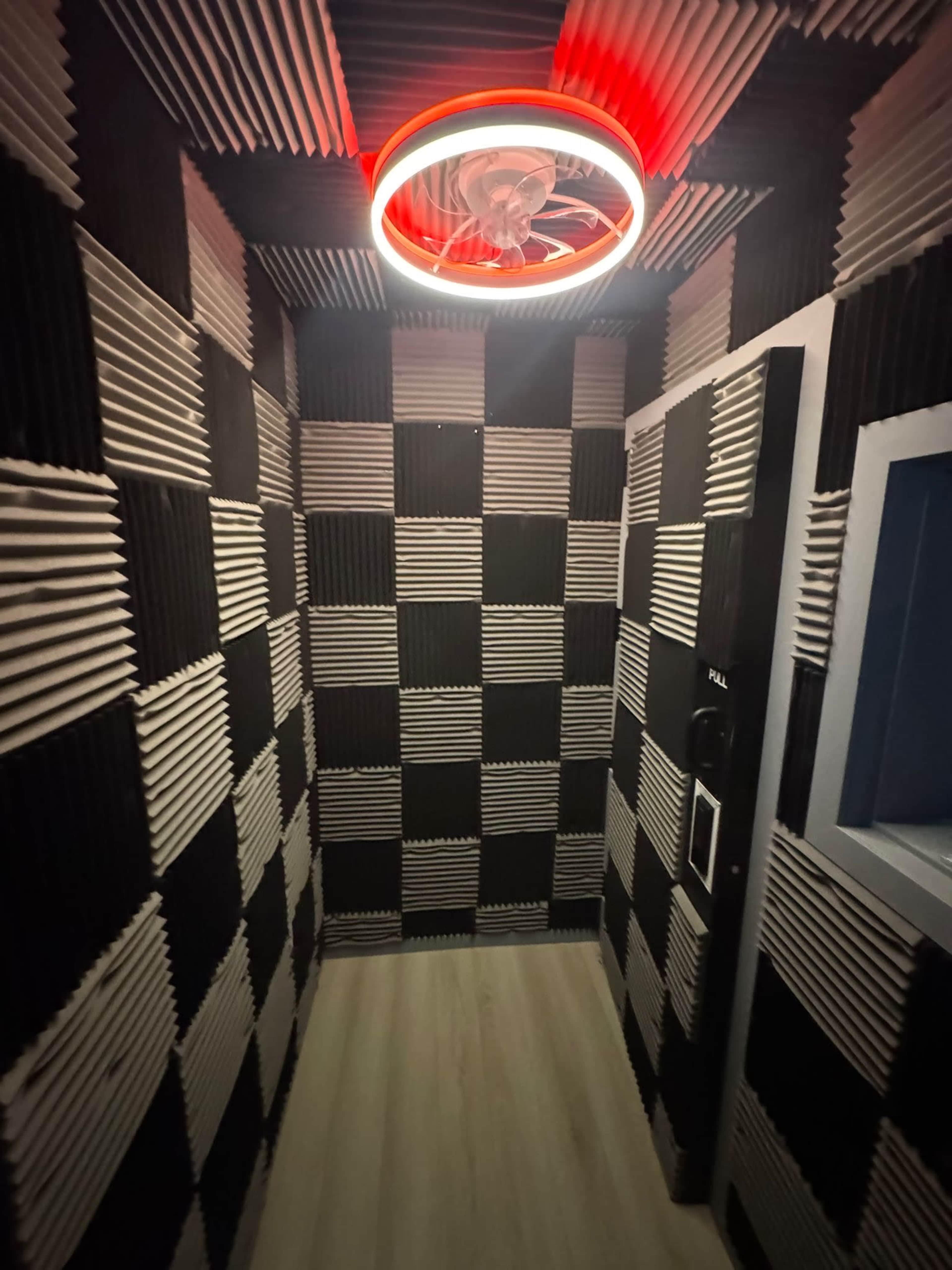 The image shows a small, enclosed room with black and white checkered acoustic paneling on the walls, and a circular light fixture with a red outer ring illuminating the space.