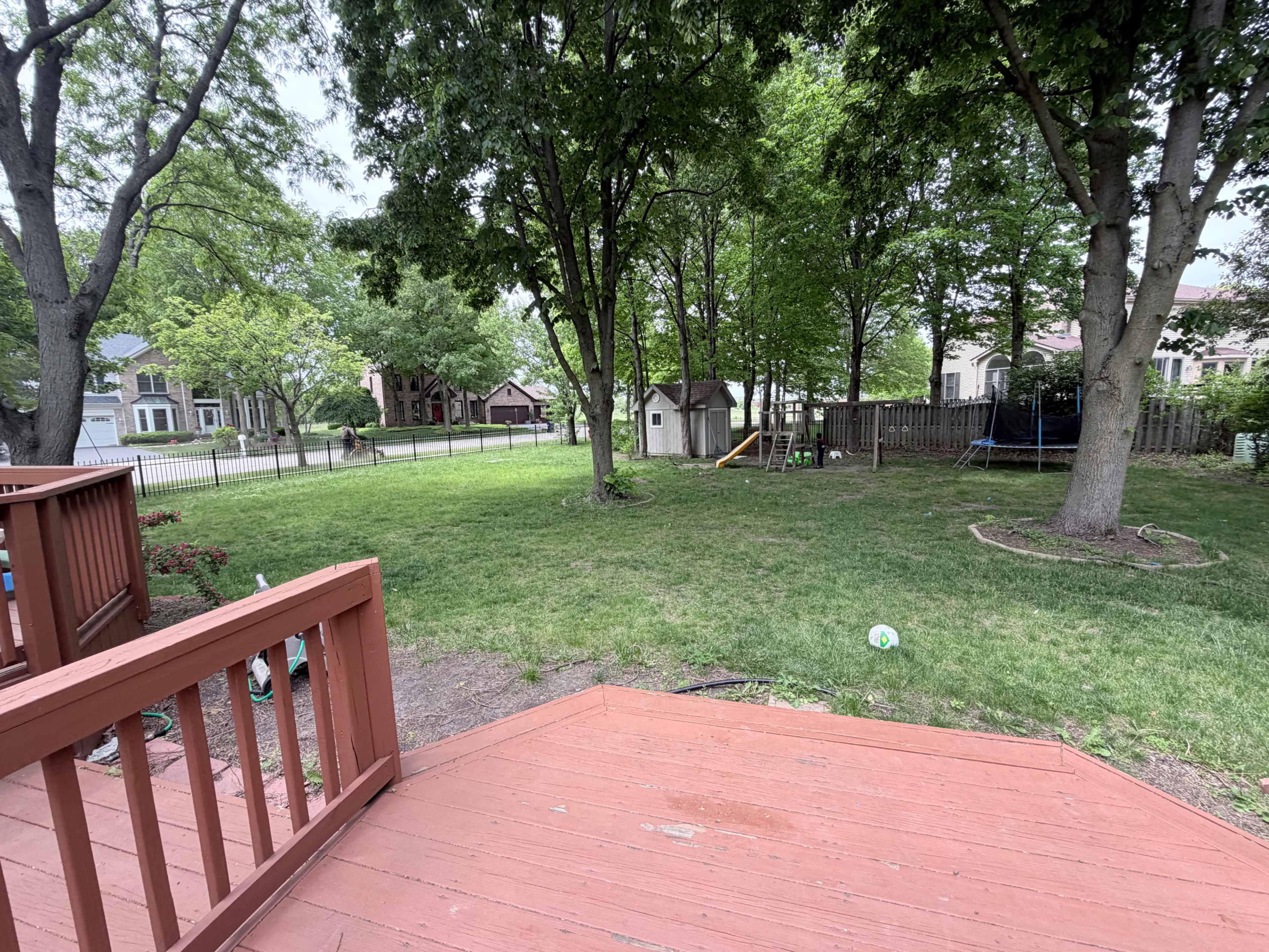 The image shows a backyard with a grassy area, a small shed, a trampoline, and a patio view from a deck.