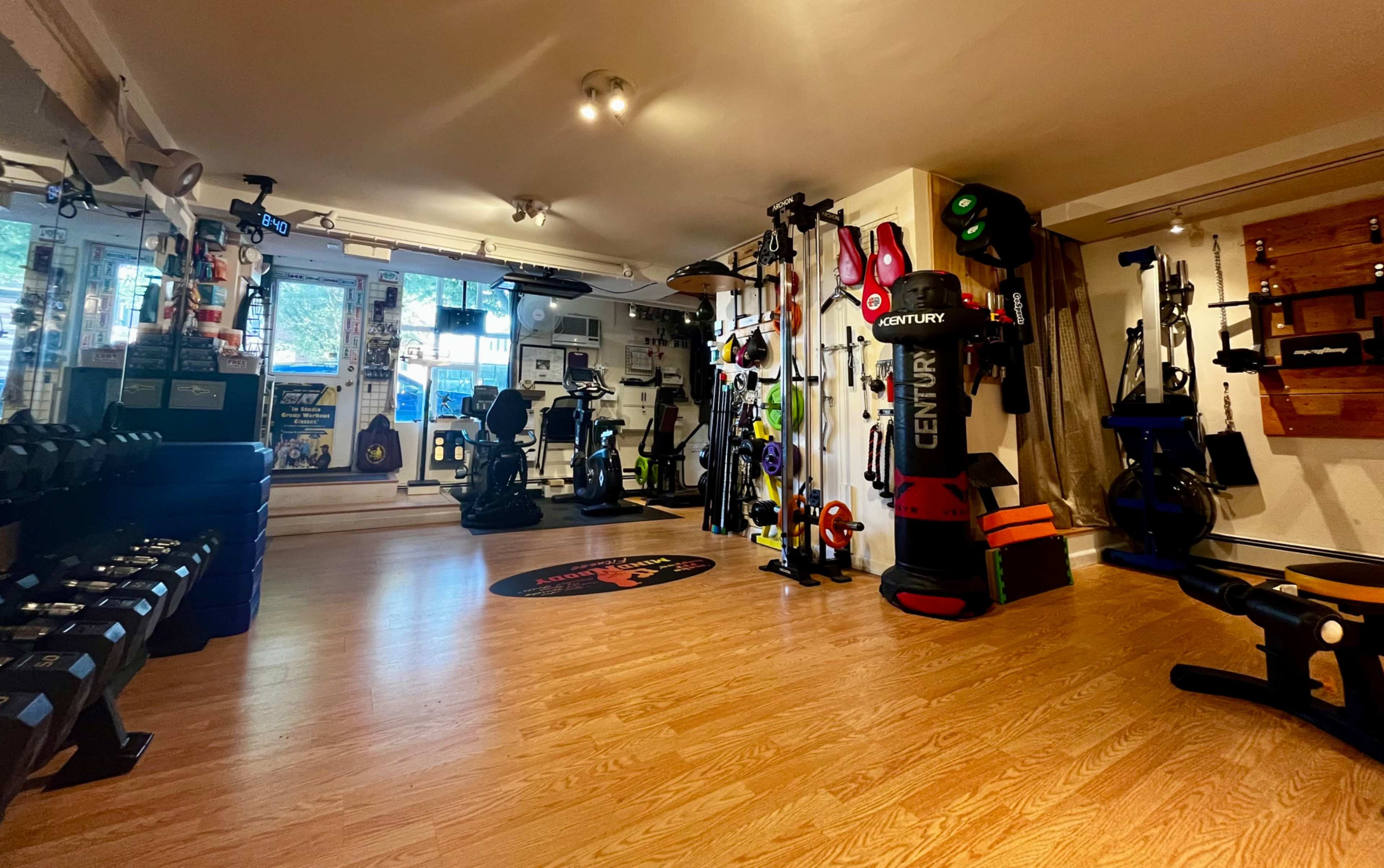 A well-equipped gym space featuring various fitness equipment, including dumbbells, exercise machines, and training tools, arranged neatly in a brightly lit room.