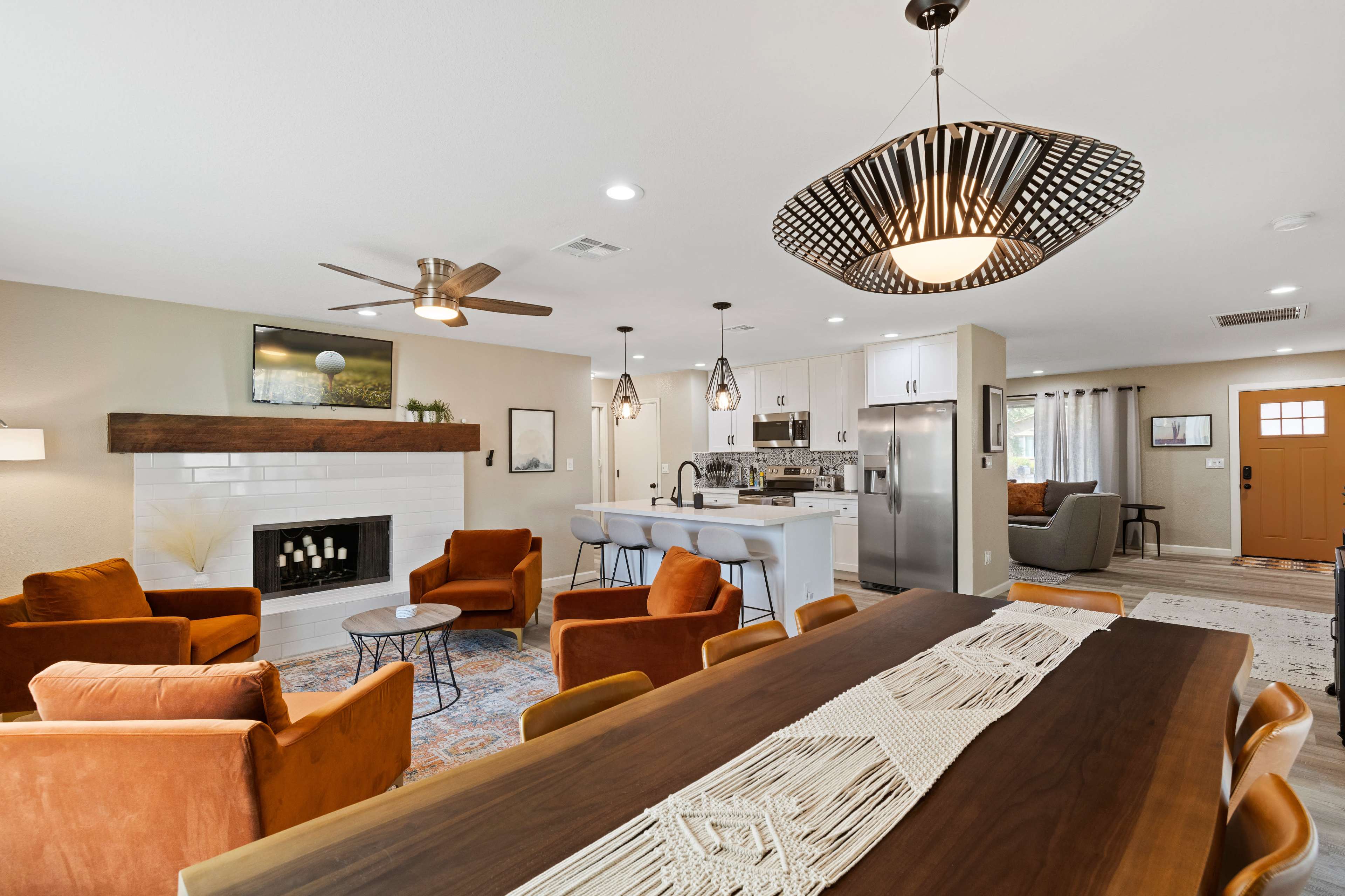 A modern living space with a dining table, orange upholstered chairs, a fireplace, and a kitchen area featuring stainless steel appliances.