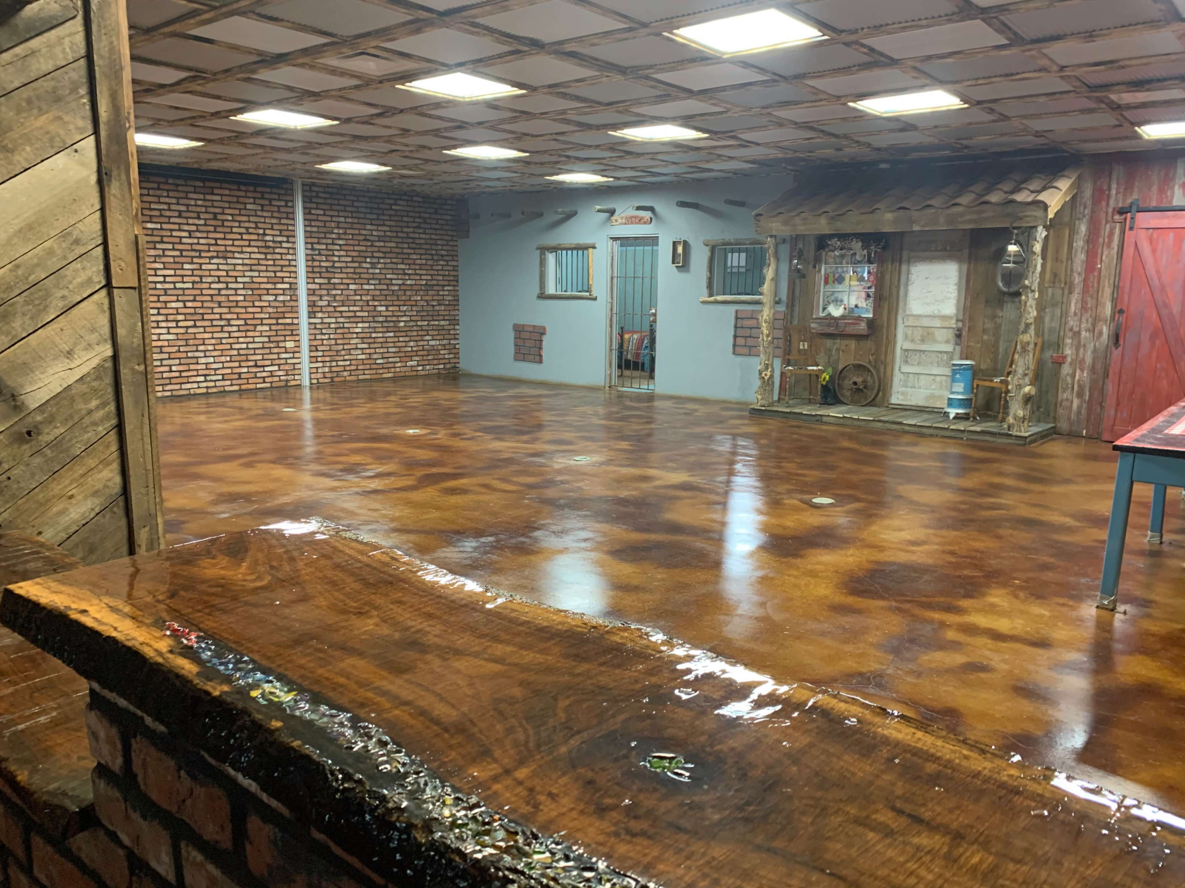 A spacious interior with polished concrete floors, exposed brick walls, and a wooden bar counter, featuring a decorative storefront structure in one corner.